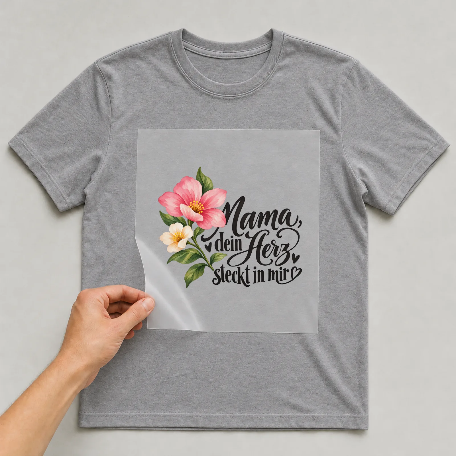 Bügelbild „Mama, dein Herz steckt in mir“ auf grauem T-Shirt, Folie wird aufgelegt