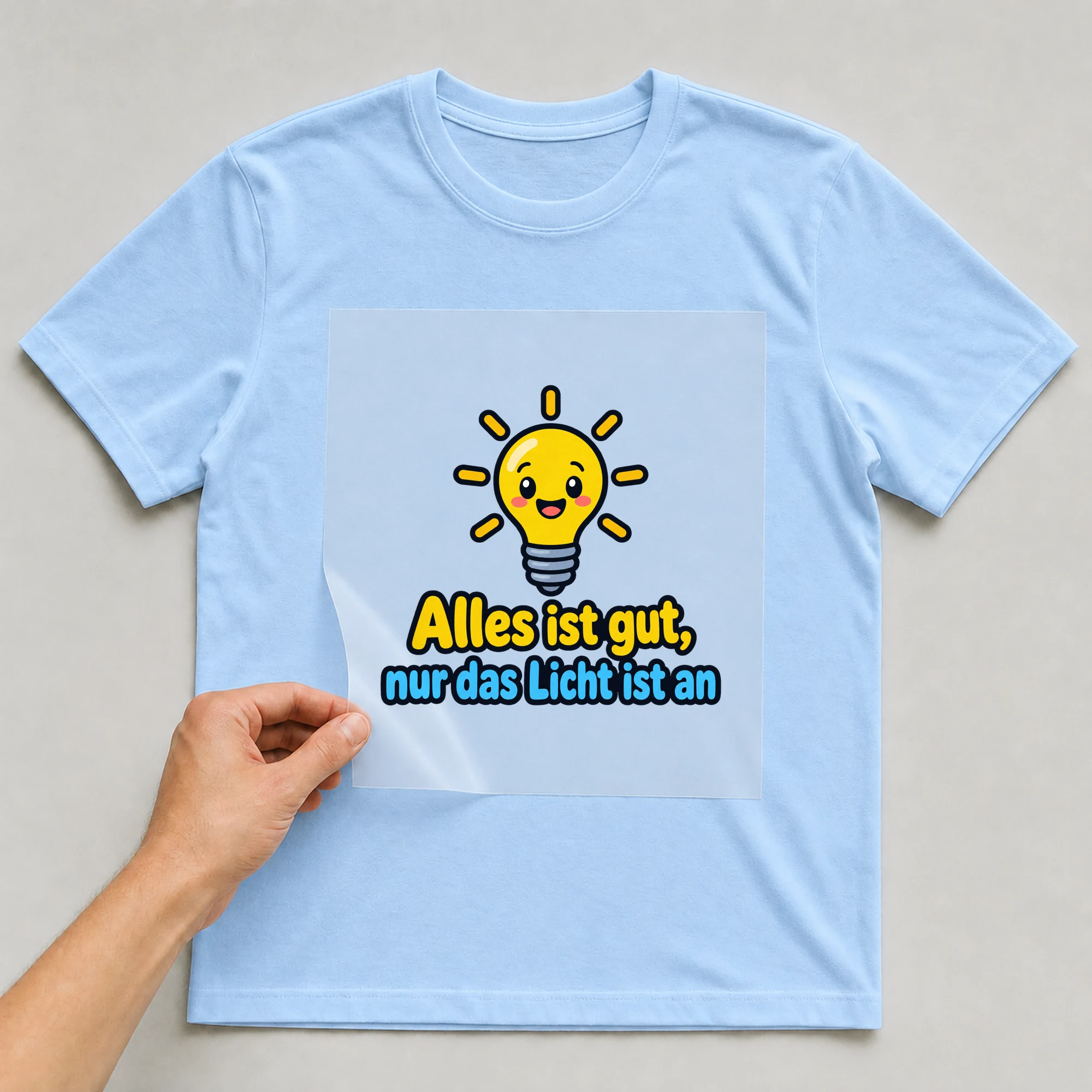 Bügelbild „Alles ist gut, nur das Licht ist an“ auf babyblauem T-Shirt, Folie wird aufgelegt