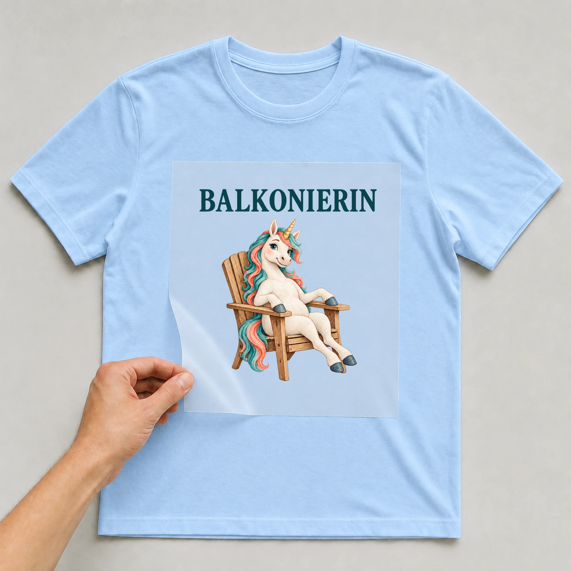 Bügelbild „BALKONIERIN“ auf babyblauem T-Shirt, Folie wird aufgelegt