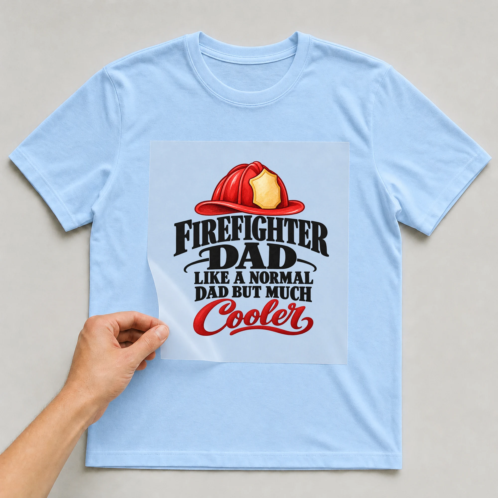 Bügelbild „Firefighter Dad Like A Normal Dad But Much Cooler“ auf babyblauem T-Shirt, Folie wird aufgelegt