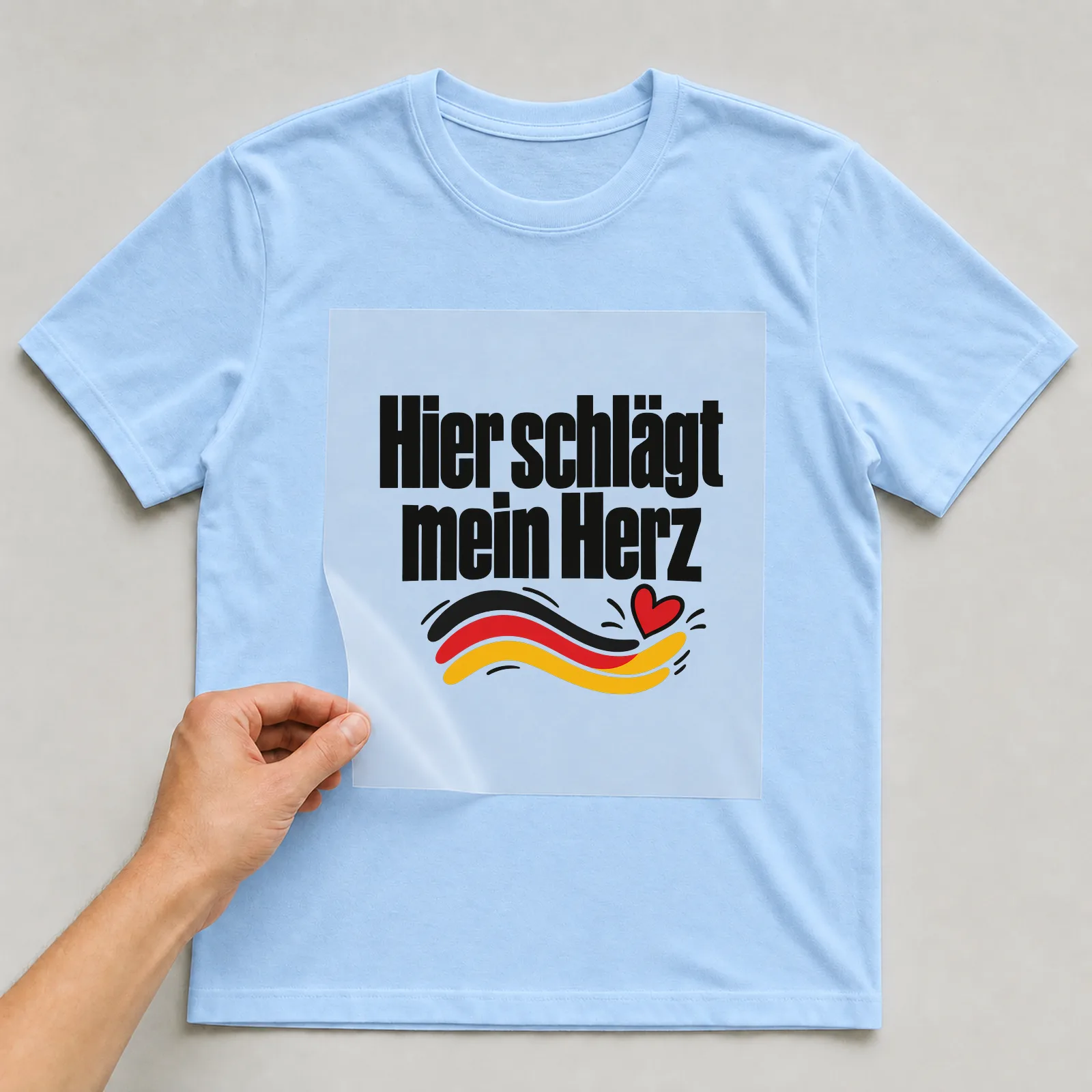 Bügelbild „Hier schlägt mein Herz“ (organischen Formen) auf hellblauem T-Shirt, Folie wird aufgelegt