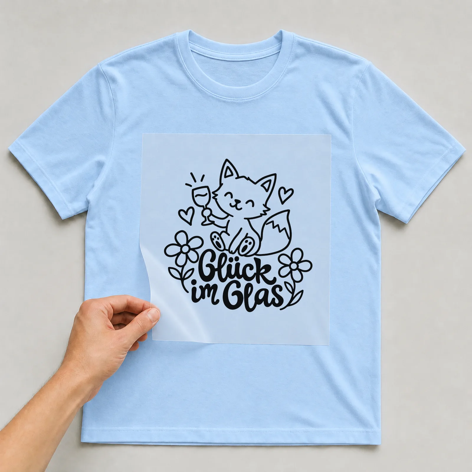 Bügelbild „Glück im Glas“ auf hellblauem T-Shirt, Folie wird aufgelegt
