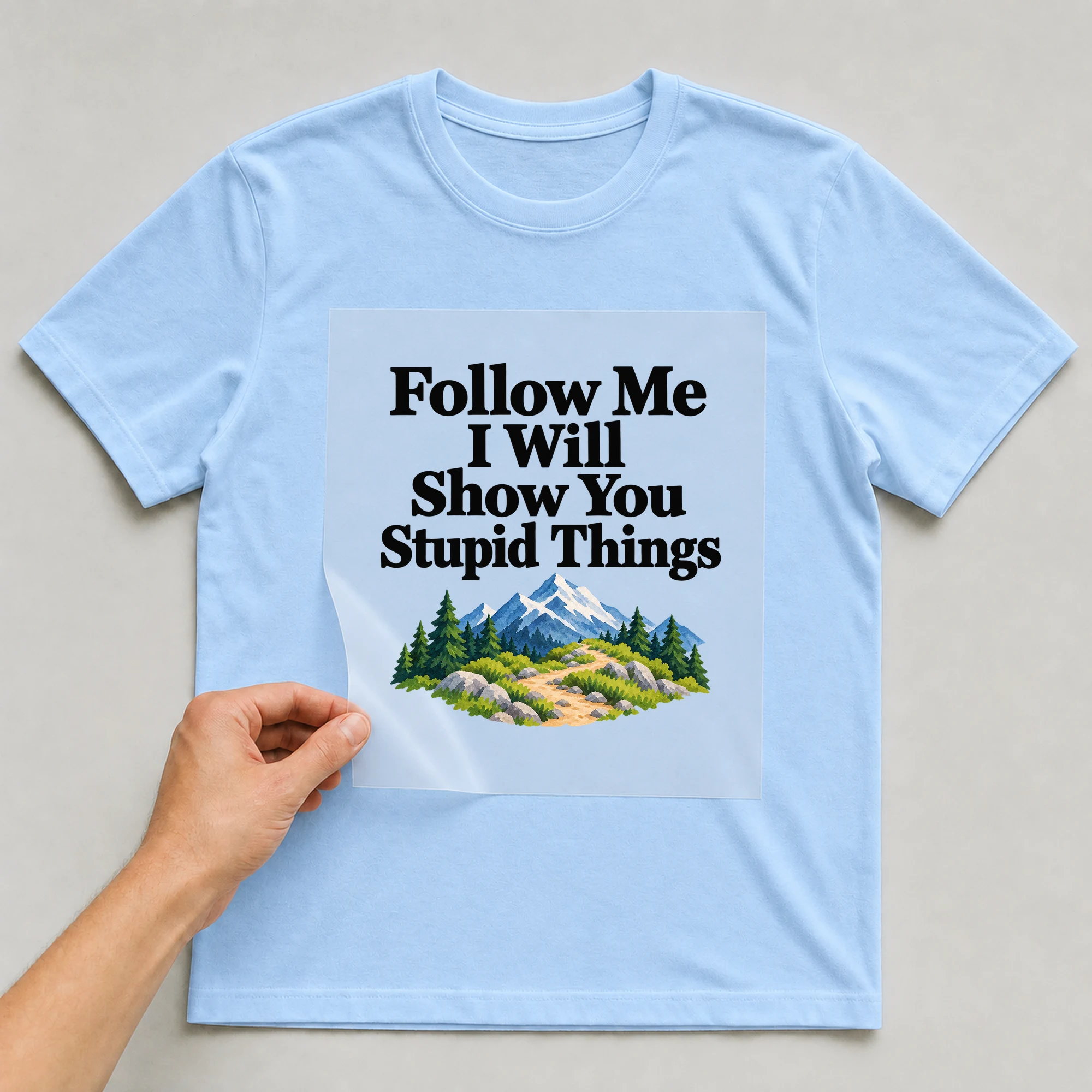 Bügelbild „Follow Me I Will Show You Stupid Things“ auf babyblauem T-Shirt, Folie wird aufgelegt