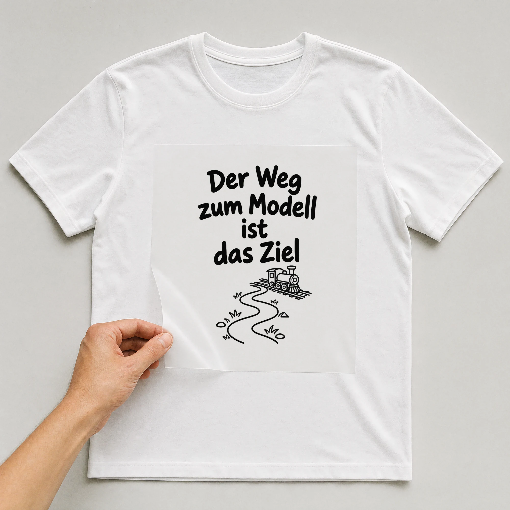 Bügelbild „Der Weg zum Modell ist das Ziel“ auf weißem T-Shirt, Folie wird aufgelegt
