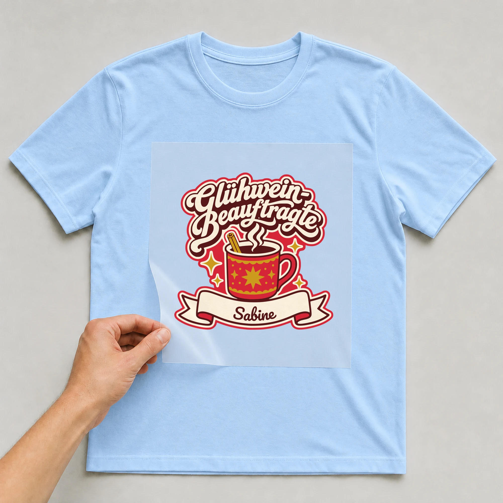 Bügelbild Glühwein-Beauftragte mit Name auf hellblauem T-Shirt, Folie wird aufgelegt
