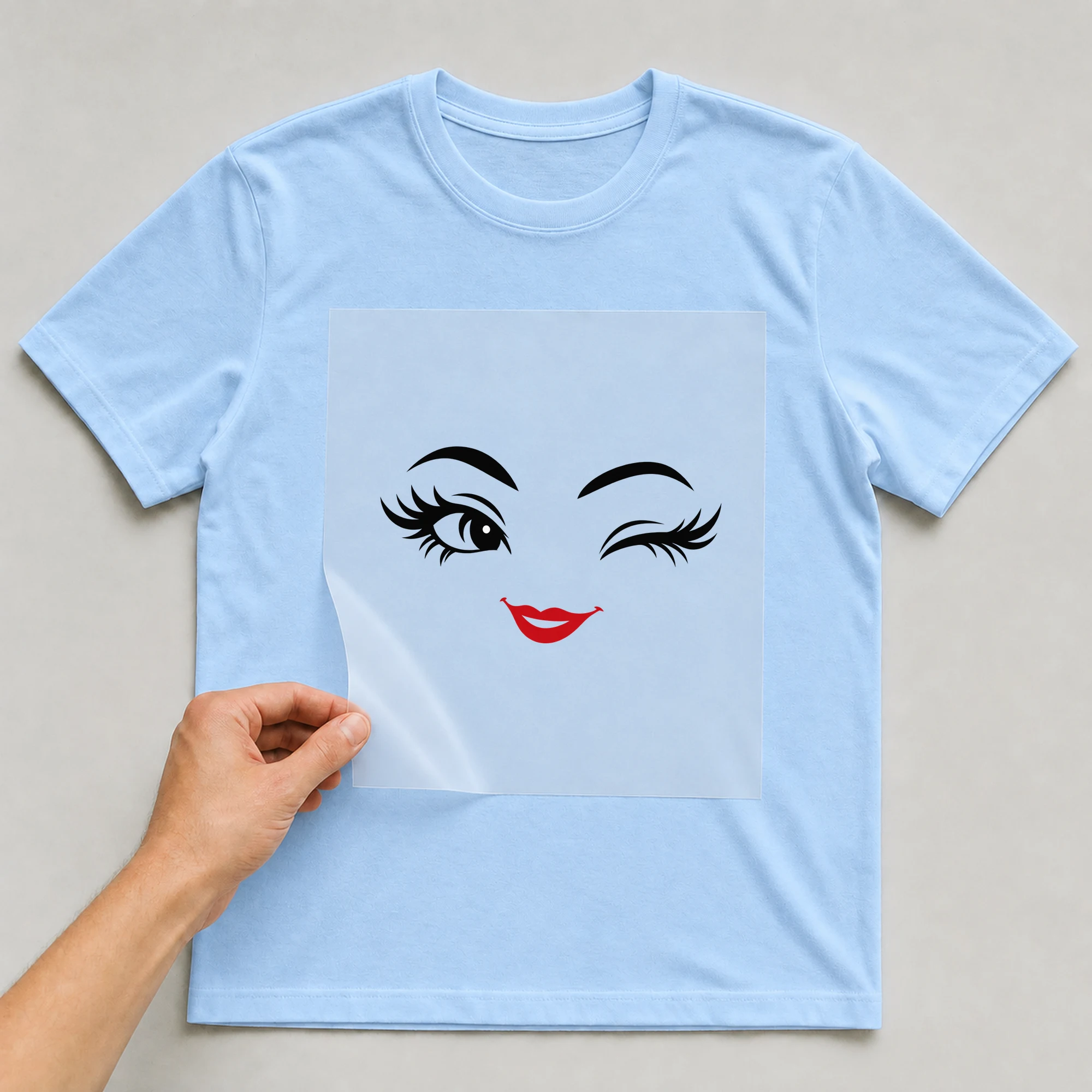 Bügelbild „Flirty Gesicht“ auf babyblauem T-Shirt, Folie wird aufgelegt