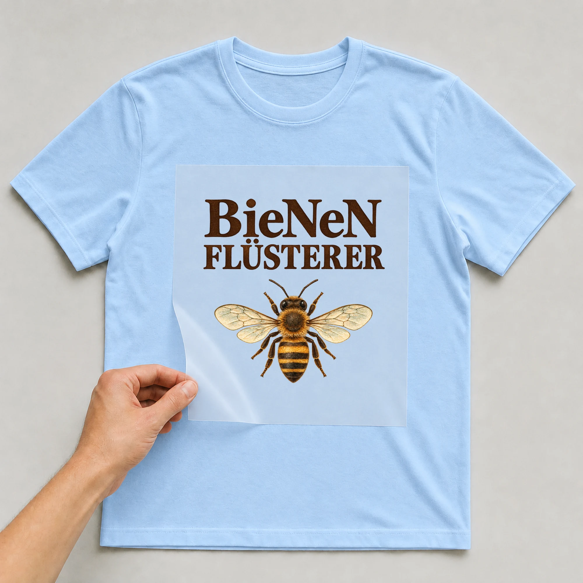 Bügelbild „BieNeN FLÜSTERER“ auf babyblauem T-Shirt, Folie wird aufgelegt
