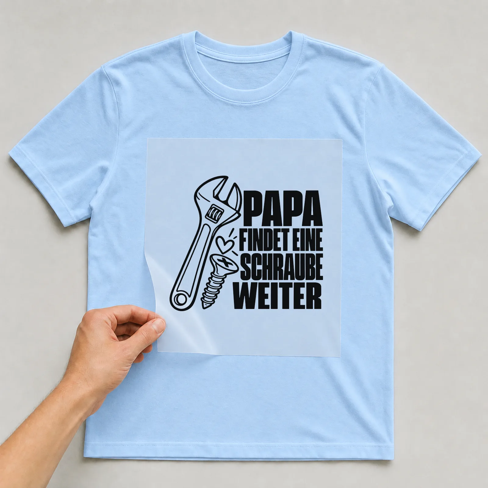 Bügelbild „Papa findet eine schraube weiter“ auf hellblauem T-Shirt, Folie wird aufgelegt