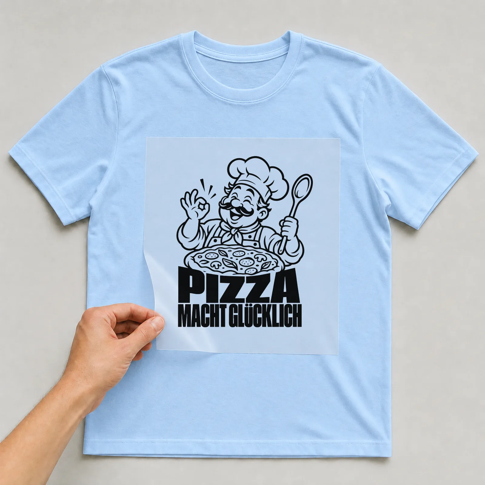Bügelbild „Pizza macht glücklich“ auf hellblauem T-Shirt, Folie wird aufgelegt