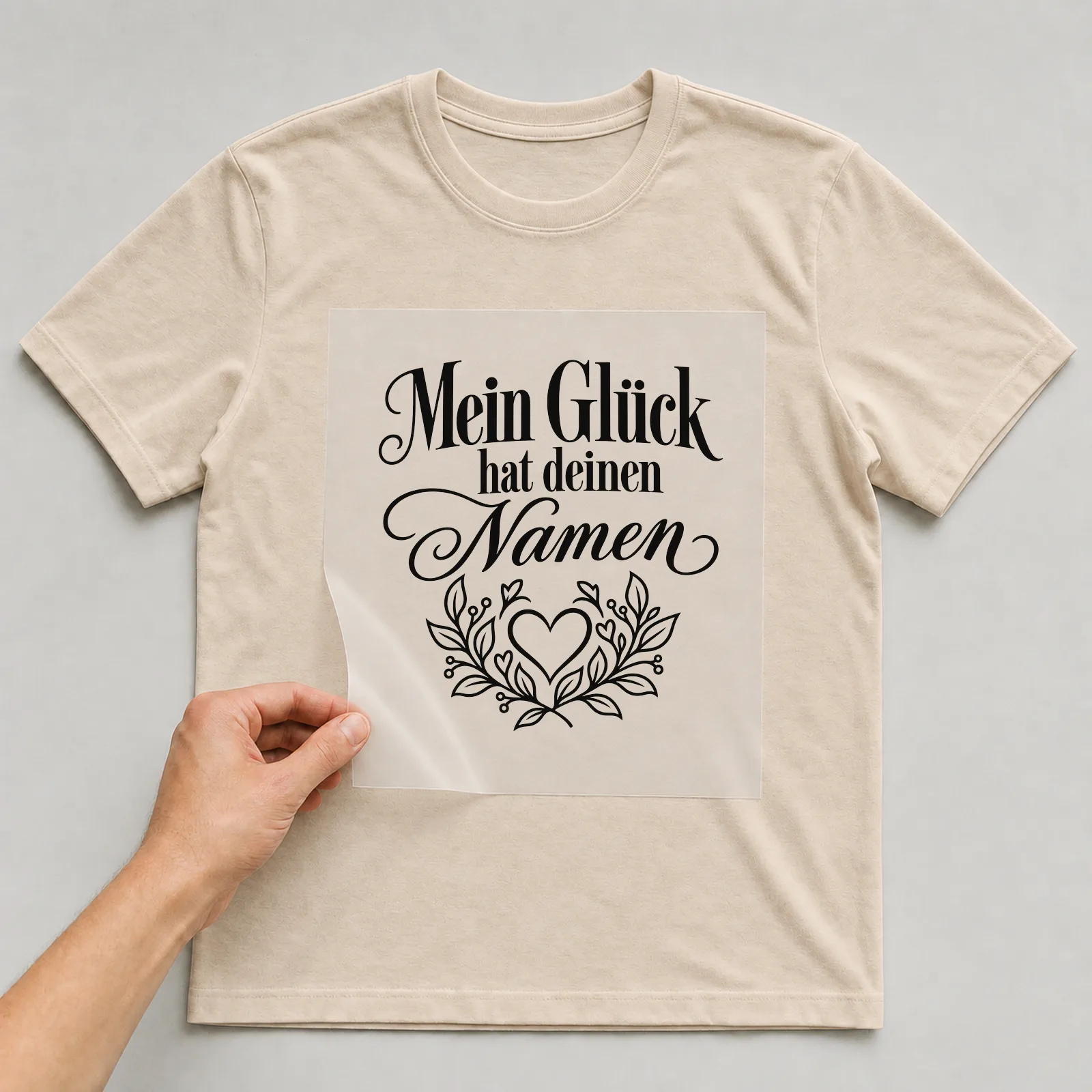 Bügelbild „Mein Glück hat deinen Namen“ auf beigem T-Shirt, Folie wird aufgelegt