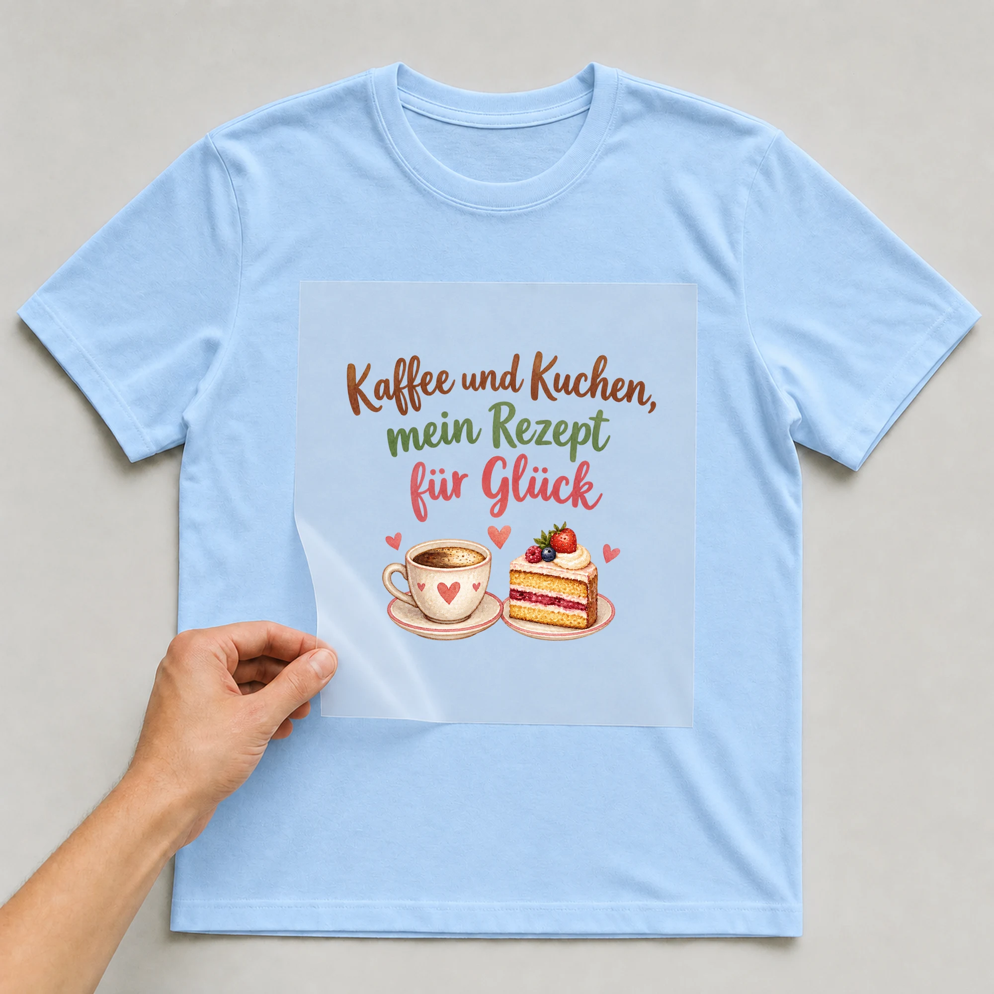Bügelbild „Kaffee und Kuchen, mein Rezept für Glück“ auf babyblauem T-Shirt, Folie wird aufgelegt
