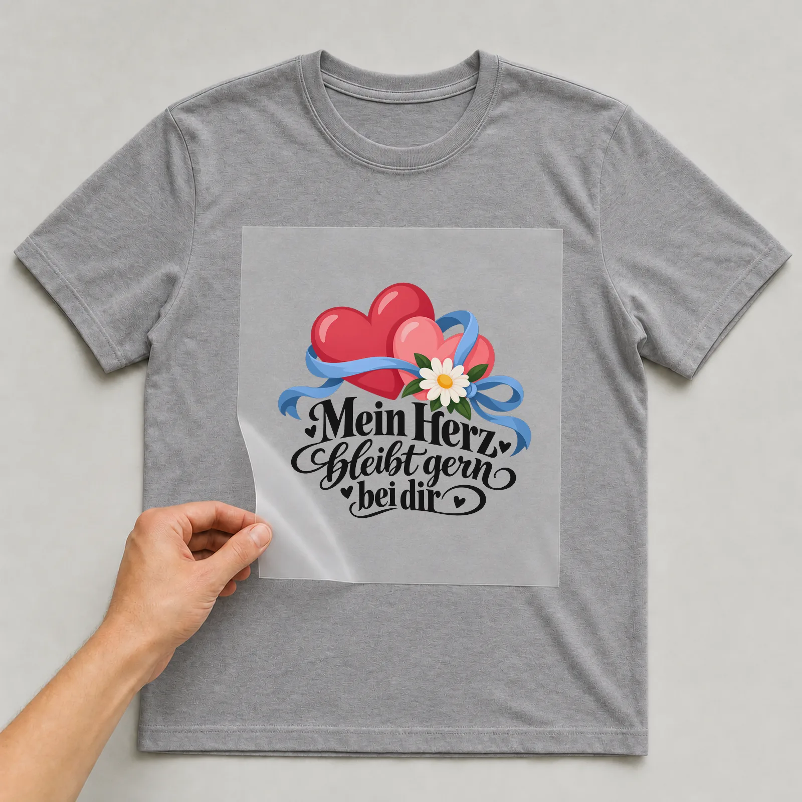 Bügelbild „Mein Herz bleibt gern bei dir“ auf grauem T-Shirt, Folie wird aufgelegt