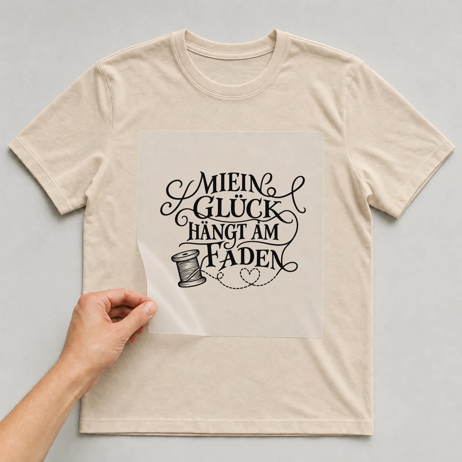 Bügelbild „Mein Glück hängt am Faden“ auf beigem T-Shirt, Folie wird aufgelegt