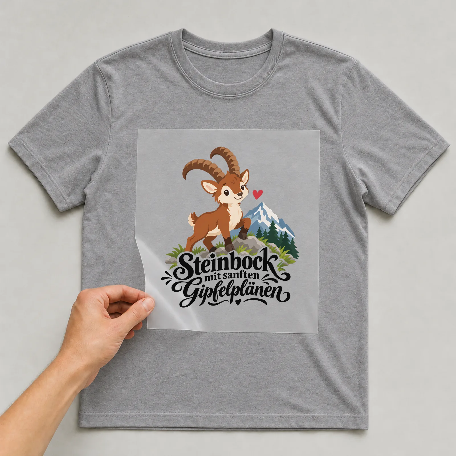 Bügelbild „Steinbock mit sanften Gipfelplänen“ auf grauem T-Shirt, Folie wird aufgelegt