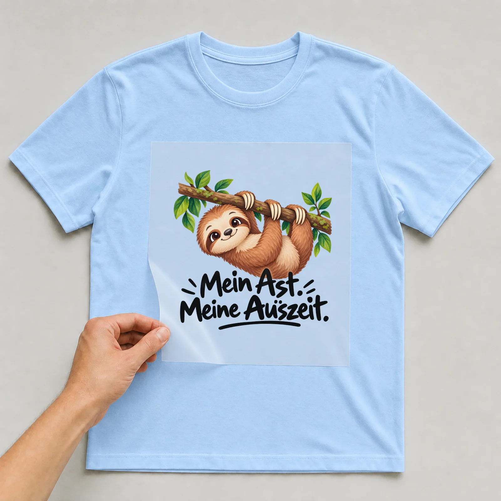 Bügelbild „Mein Ast. Meine Auszeit.“ auf hellblauem T-Shirt, Folie wird aufgelegt