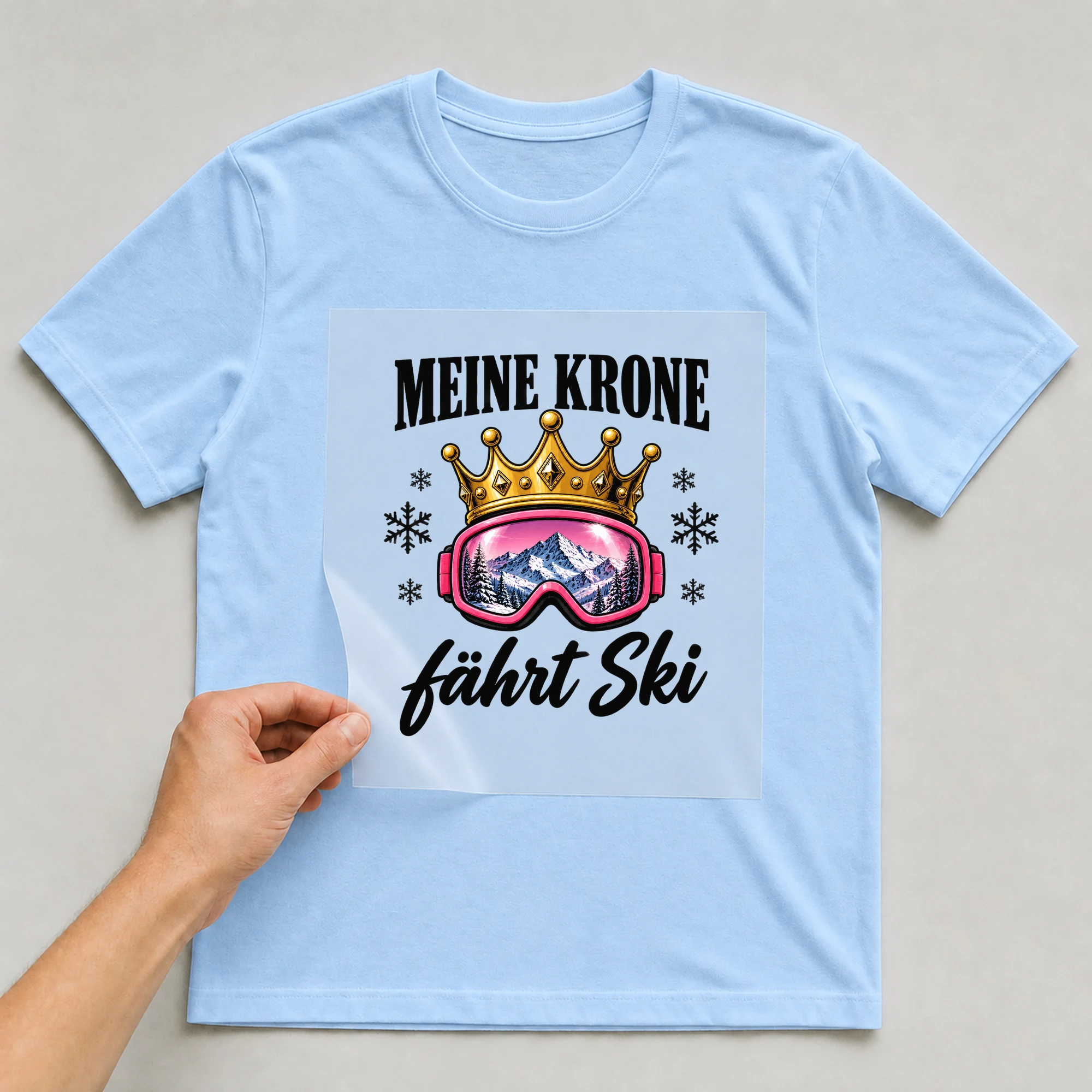 Bügelbild „Meine Krone fährt Ski“ auf hellblauem T-Shirt, Folie wird aufgelegt