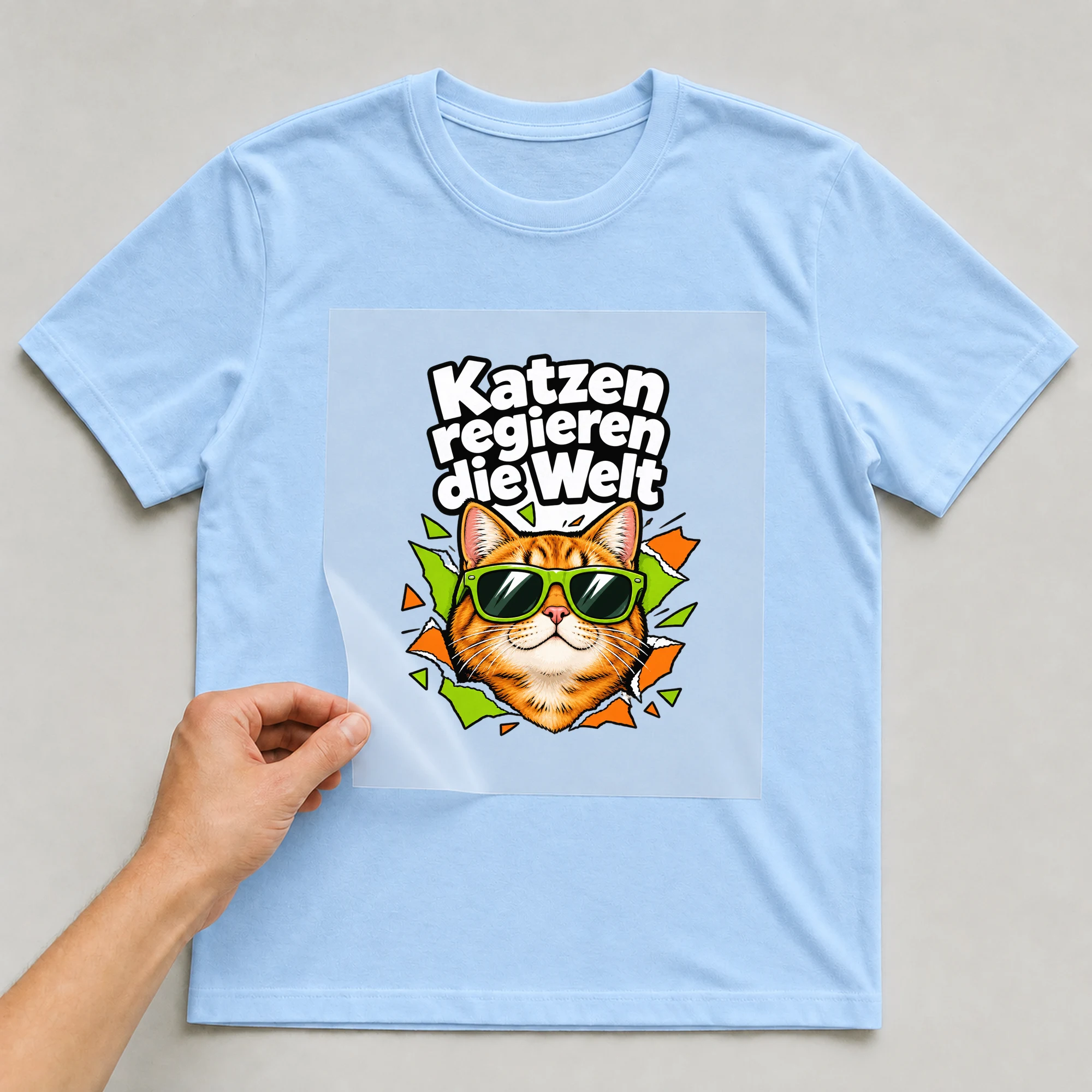 Bügelbild „Katzen regieren die Welt“ auf babyblauem T-Shirt, Folie wird aufgelegt
