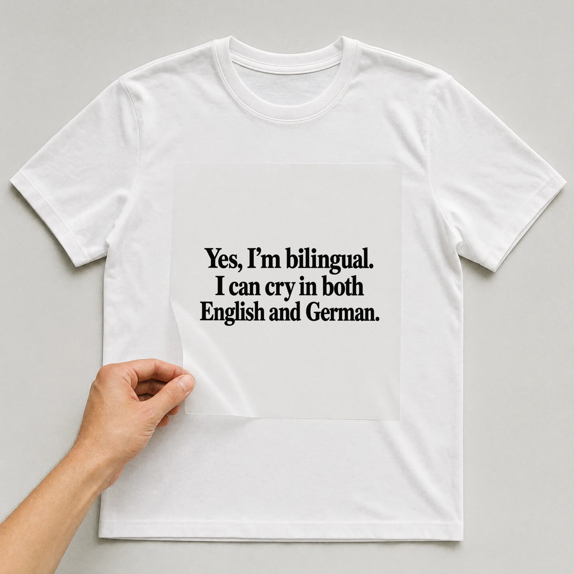 Bügelbild „Yes, I'm bilingual. I can cry in both English and German.“ auf weißem T-Shirt, Folie wird aufgelegt