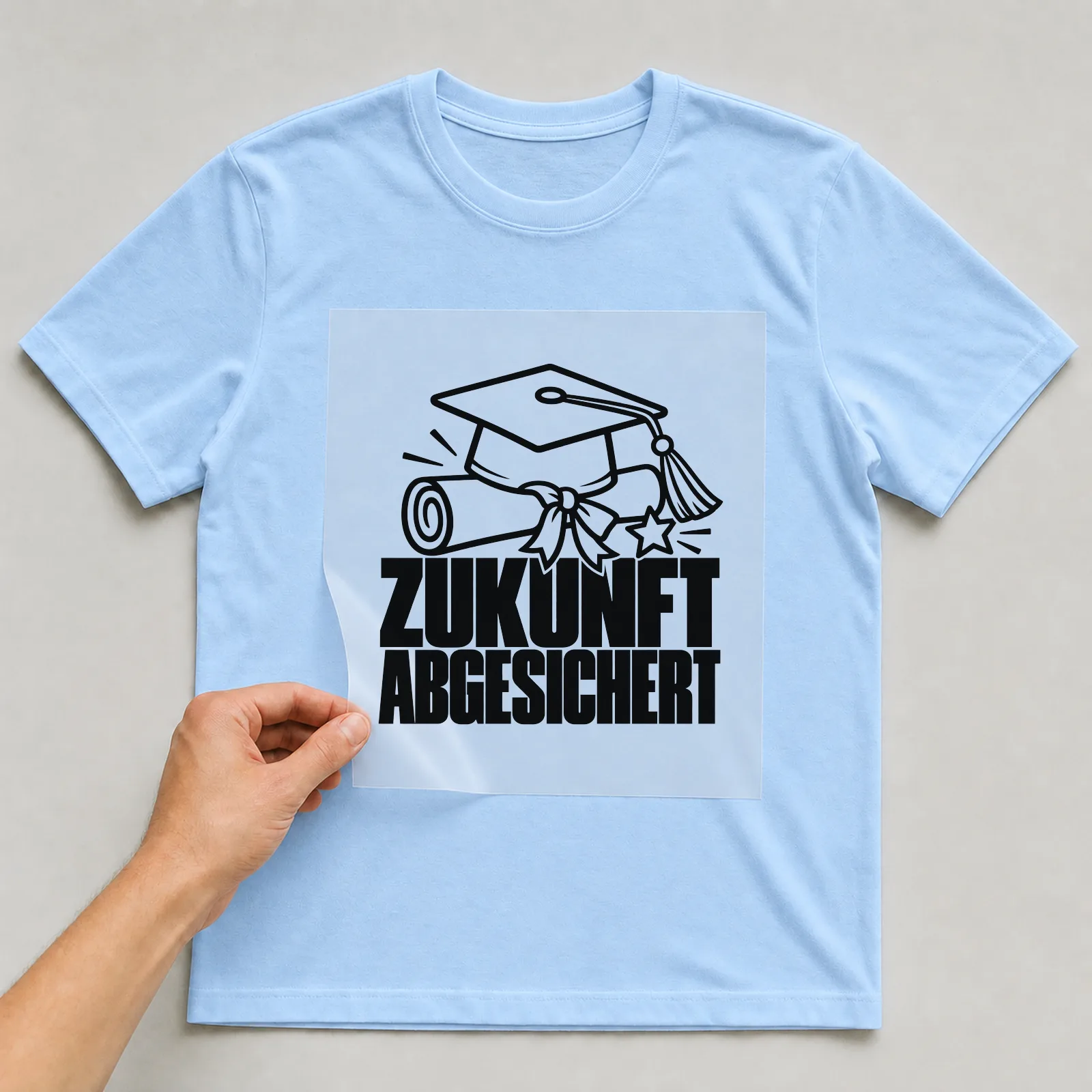 Bügelbild „Zukunft abgesichert“ auf hellblauem T-Shirt, Folie wird aufgelegt