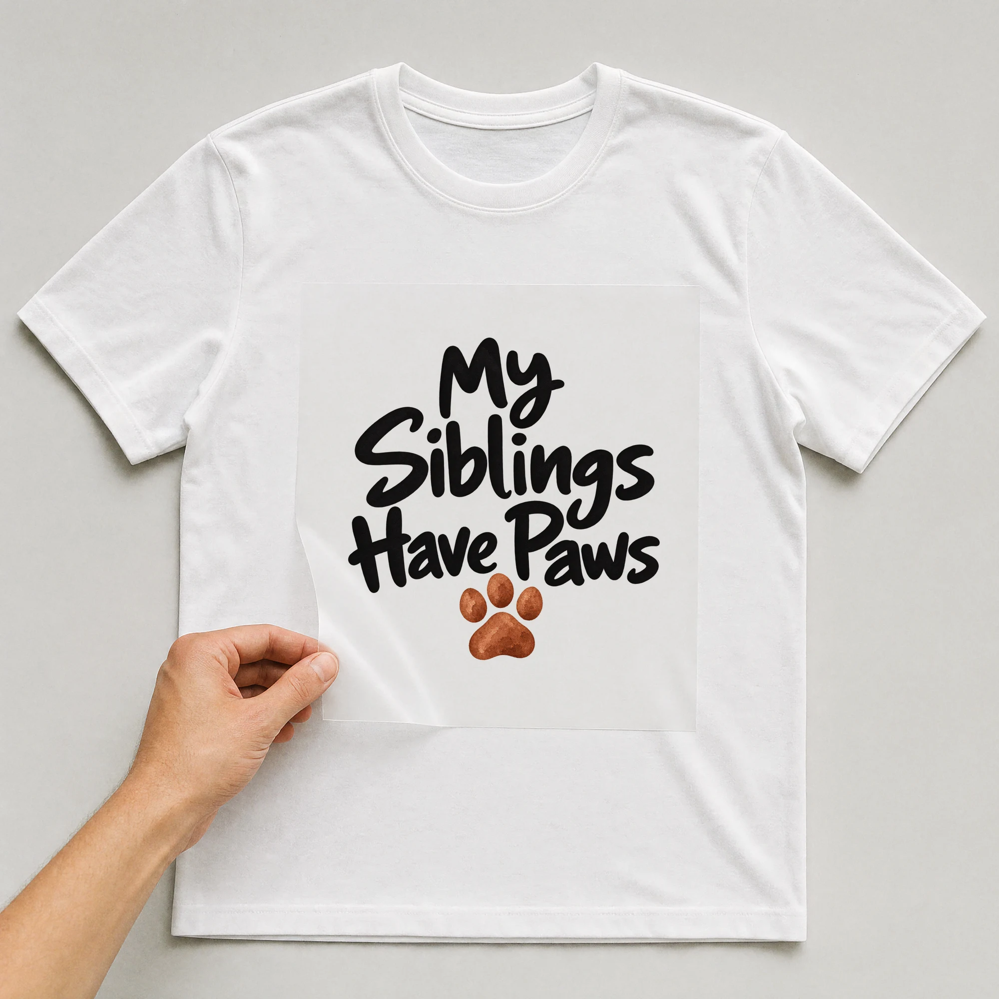Bügelbild „My Siblings Have Paws“ auf weißem T-Shirt, Folie wird aufgelegt