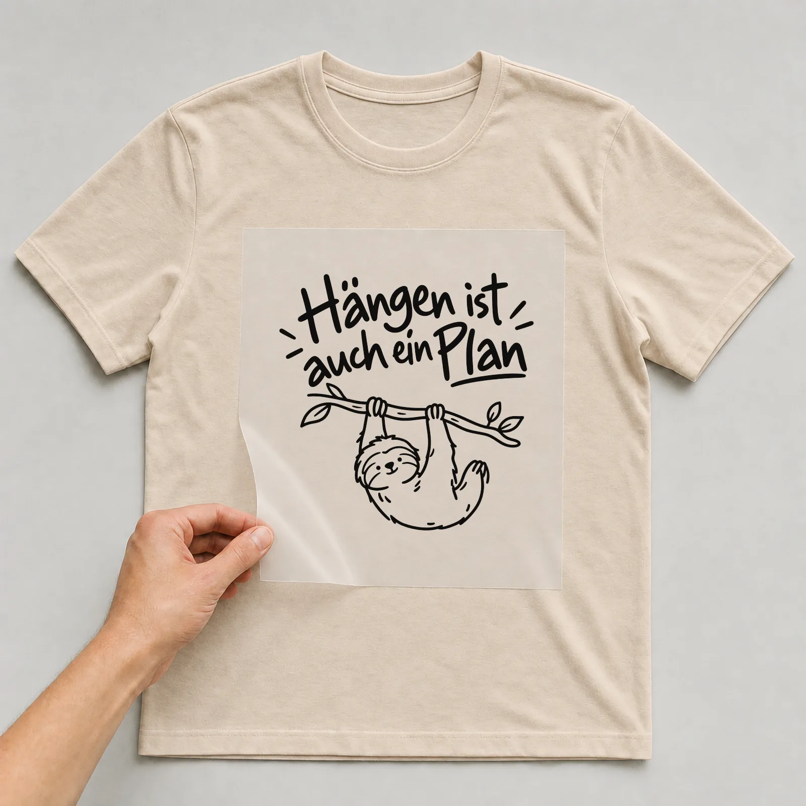 Bügelbild „Hängen ist auch ein Plan“ auf beigem T-Shirt, Folie wird aufgelegt