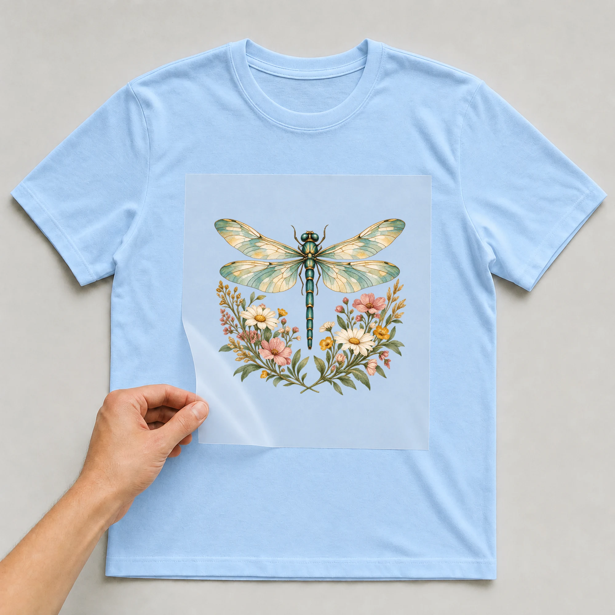Bügelbild „Libelle auf der Wiese“ auf babyblauem T-Shirt, Folie wird aufgelegt