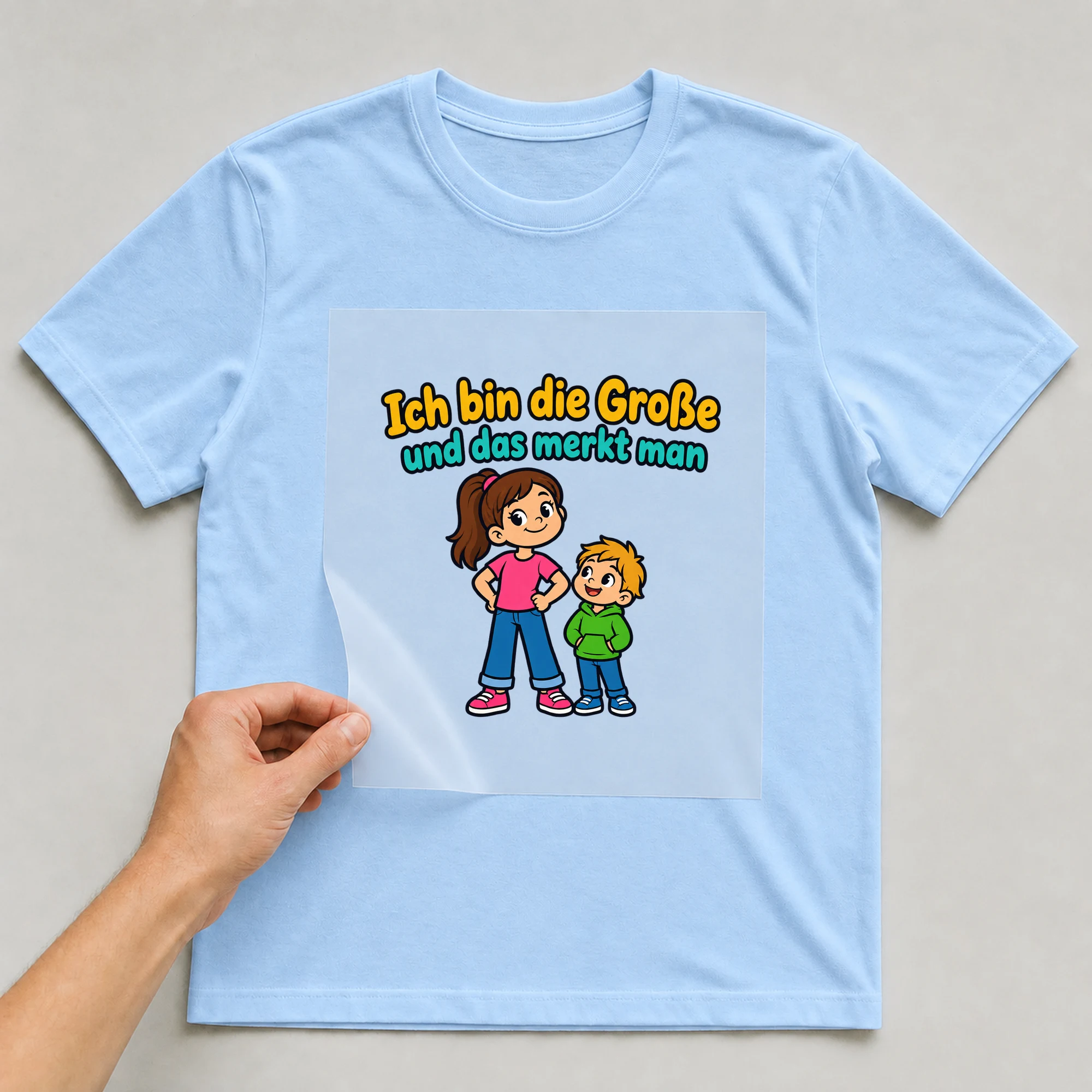 Bügelbild „Ich bin die Große und das merkt man“ auf babyblauem T-Shirt, Folie wird aufgelegt