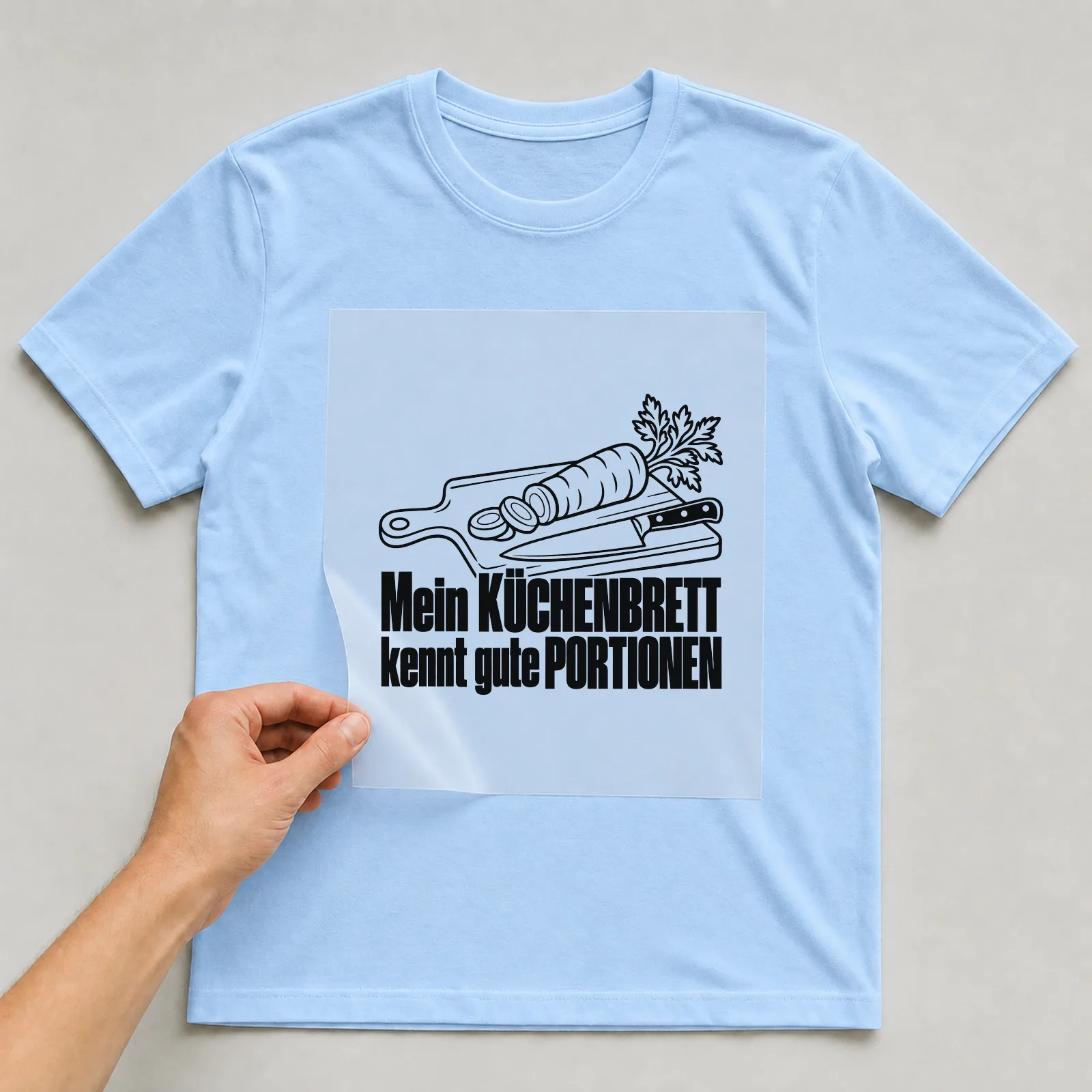 Bügelbild „Mein KÜCHENBRETT kennt gute PORTIONEN“ auf hellblauem T-Shirt, Folie wird aufgelegt