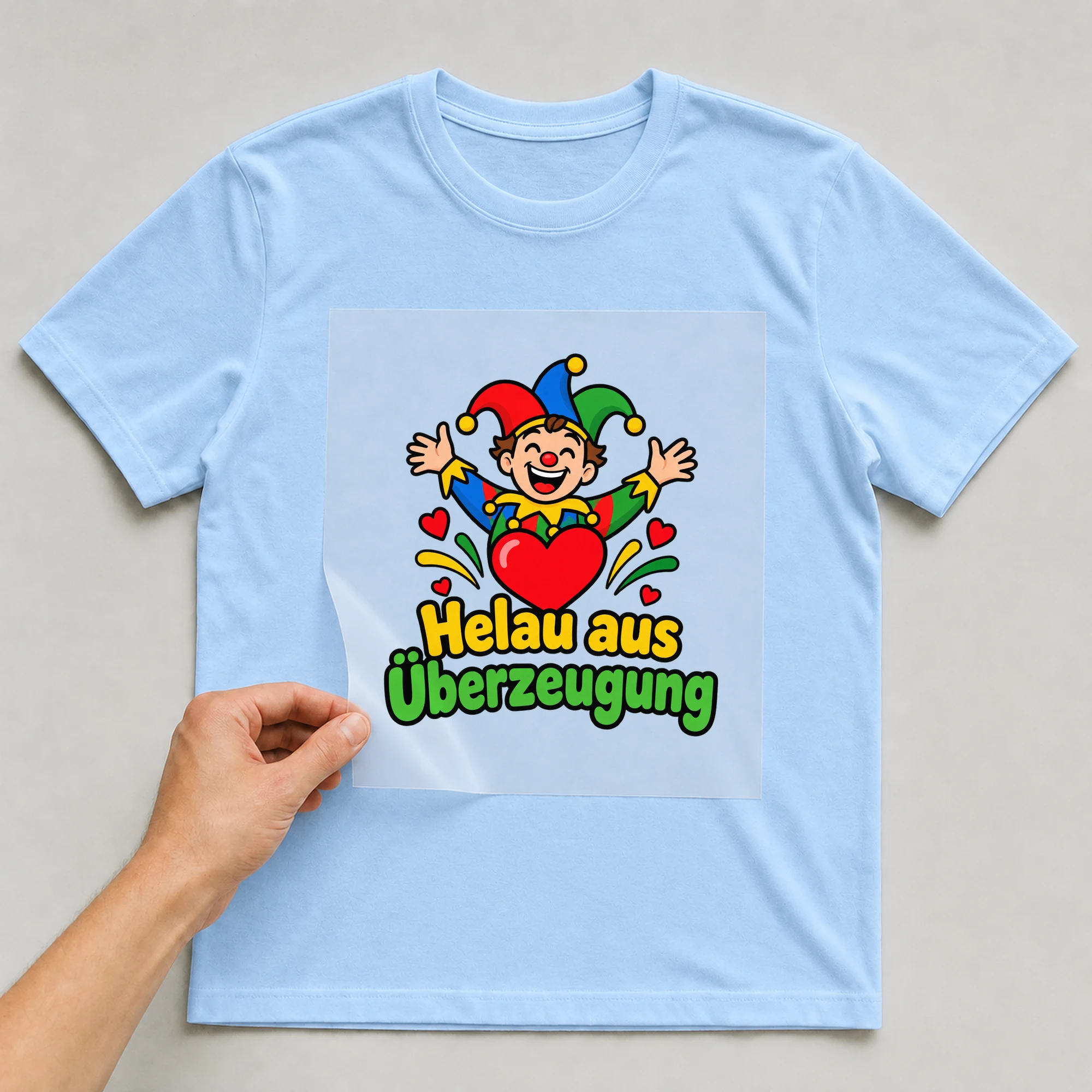 Bügelbild „Helau aus Überzeugung“ auf babyblauem T-Shirt, Folie wird aufgelegt