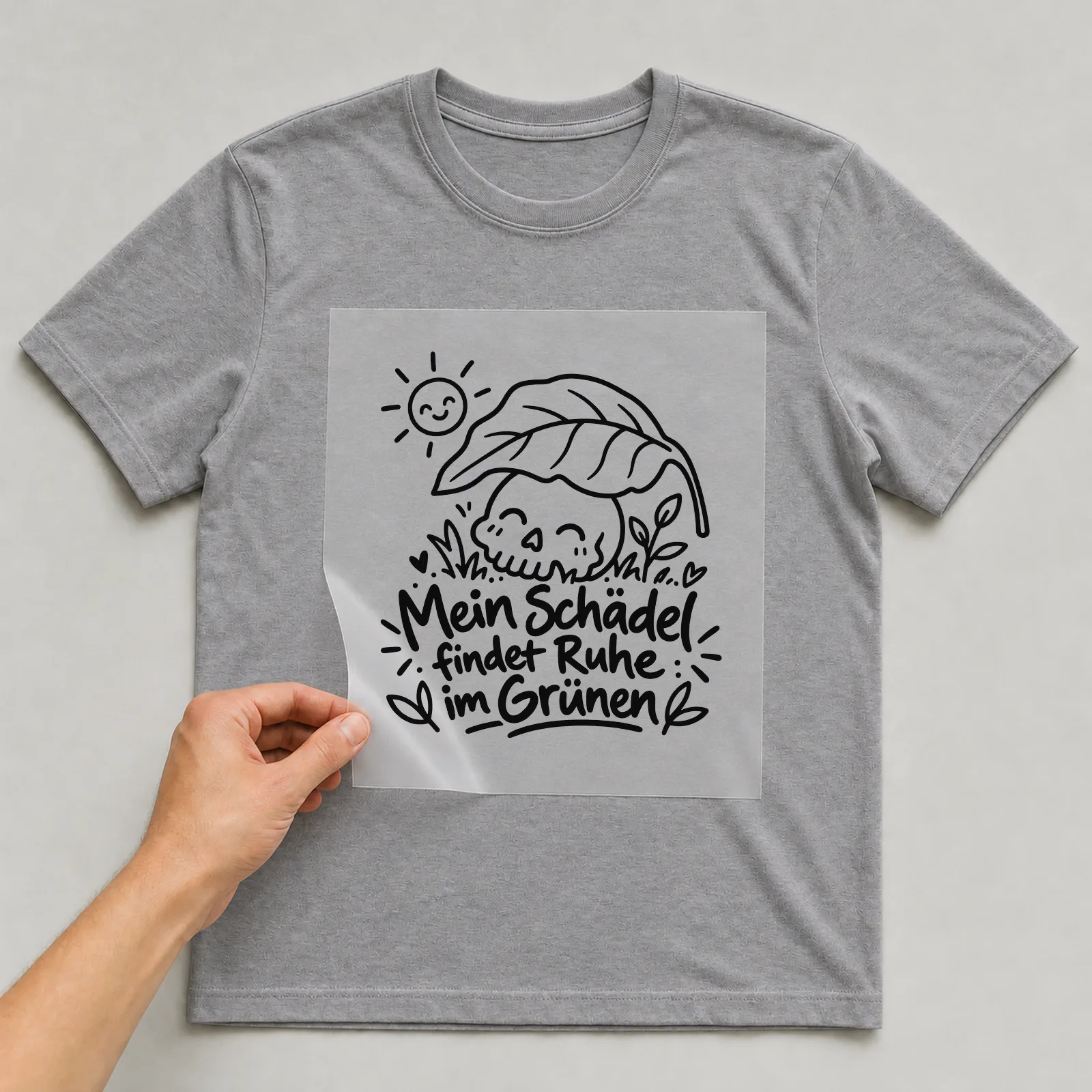 Bügelbild „Mein Schädel findet Ruhe im Grünen“ auf grauem T-Shirt, Folie wird aufgelegt