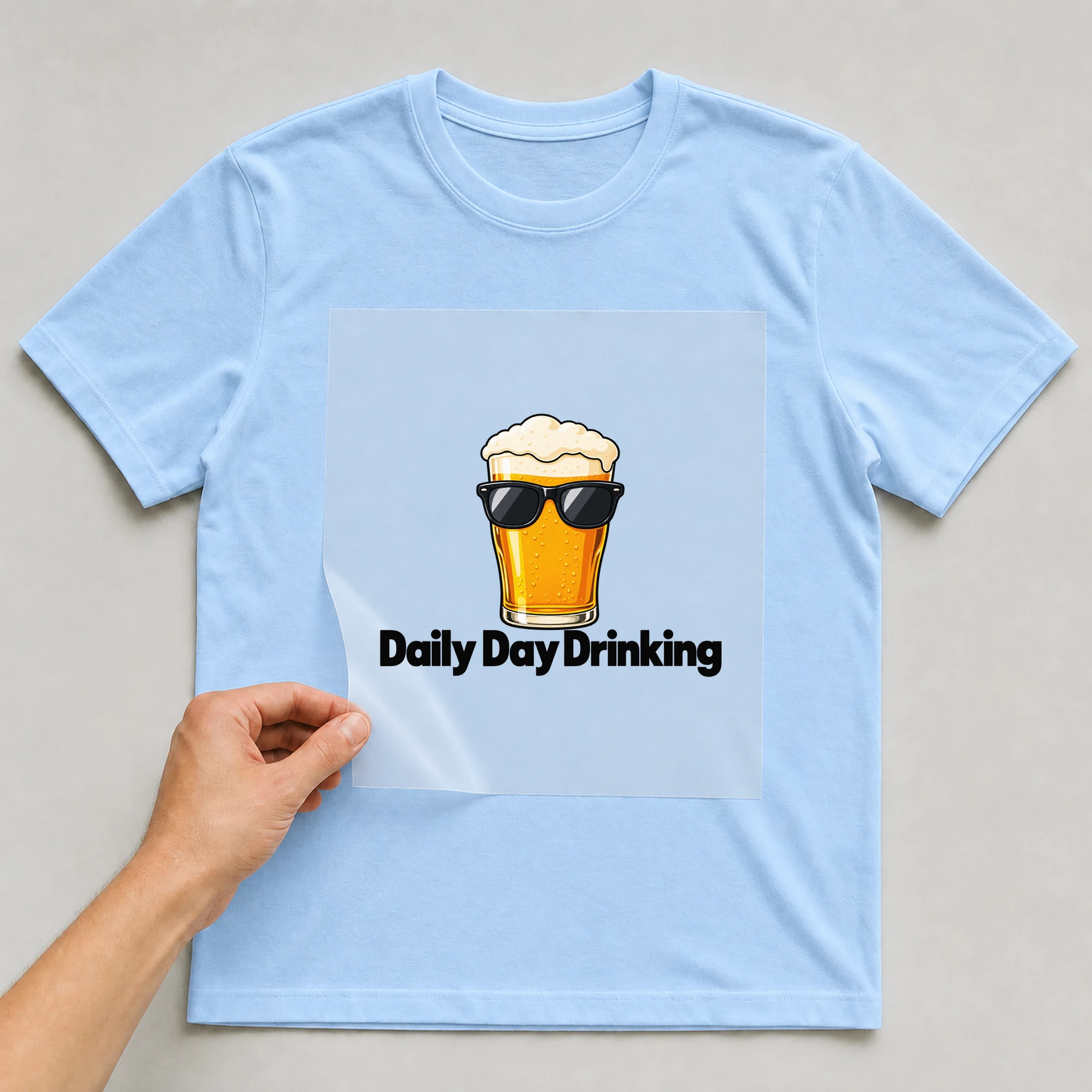 Bügelbild „Daily Day Drinking“ auf babyblauem T-Shirt, Folie wird aufgelegt