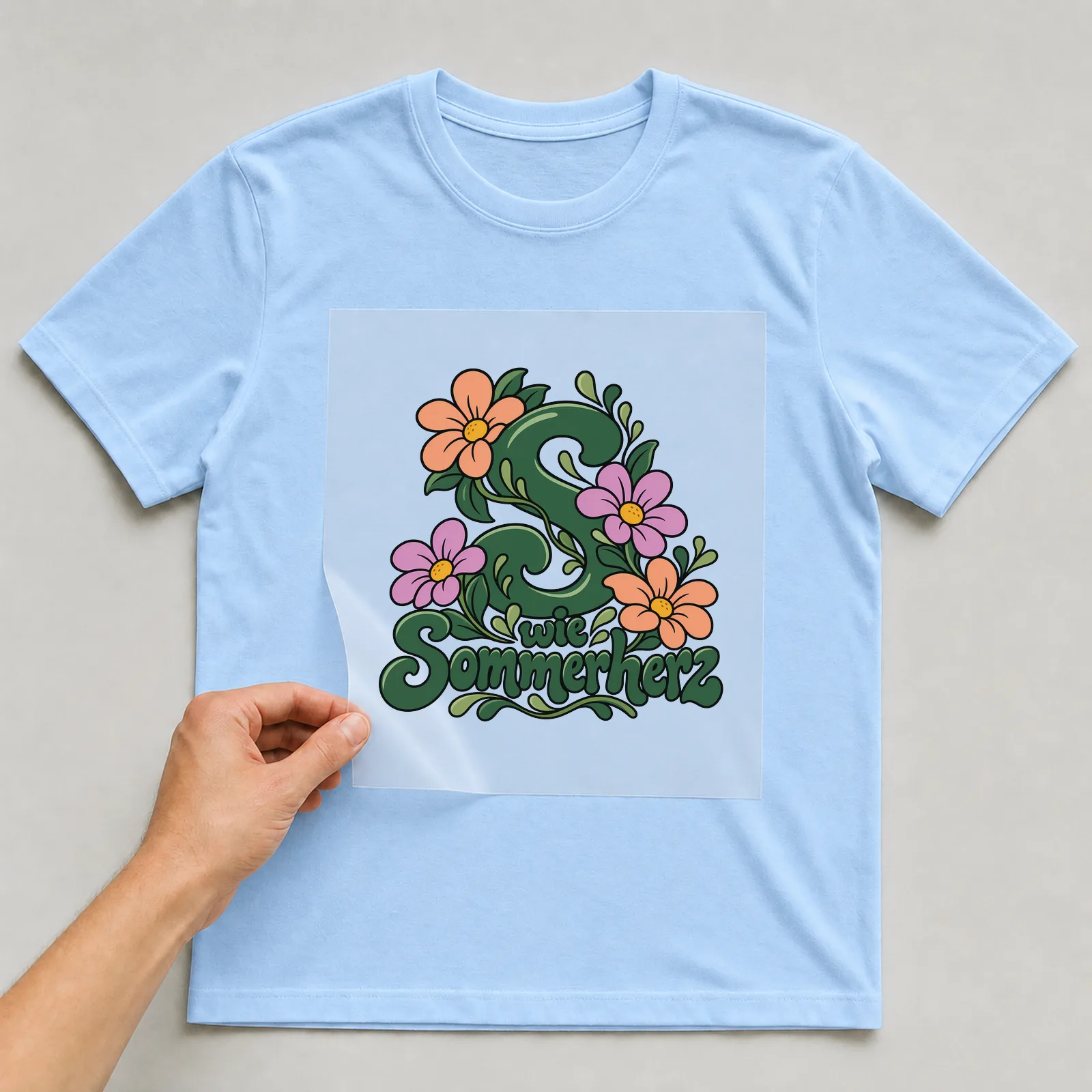 Bügelbild „S wie Sommerherz“ auf hellblauem T-Shirt, Folie wird aufgelegt