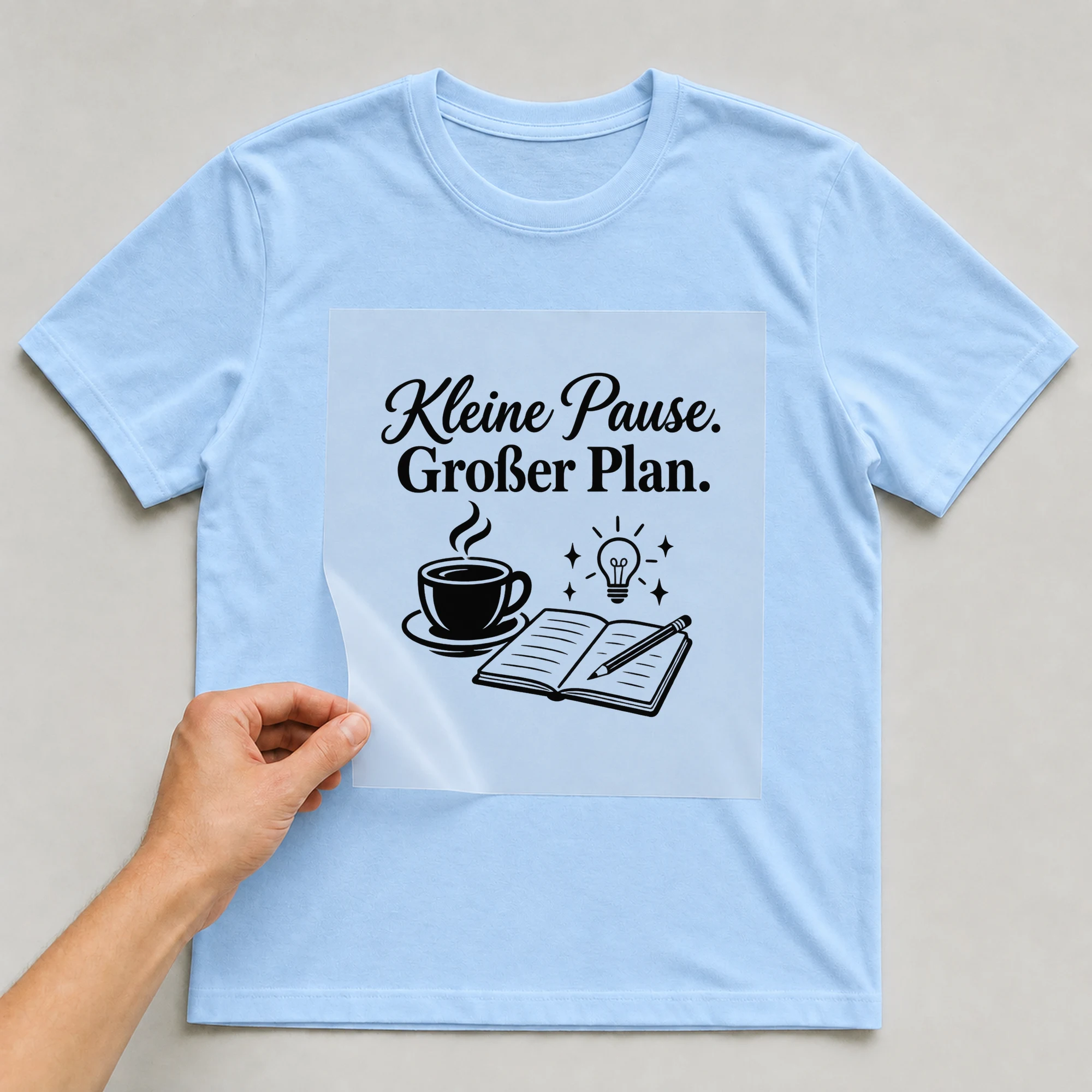 Bügelbild „Kleine Pause. Großer Plan.“ auf babyblauem T-Shirt, Folie wird aufgelegt