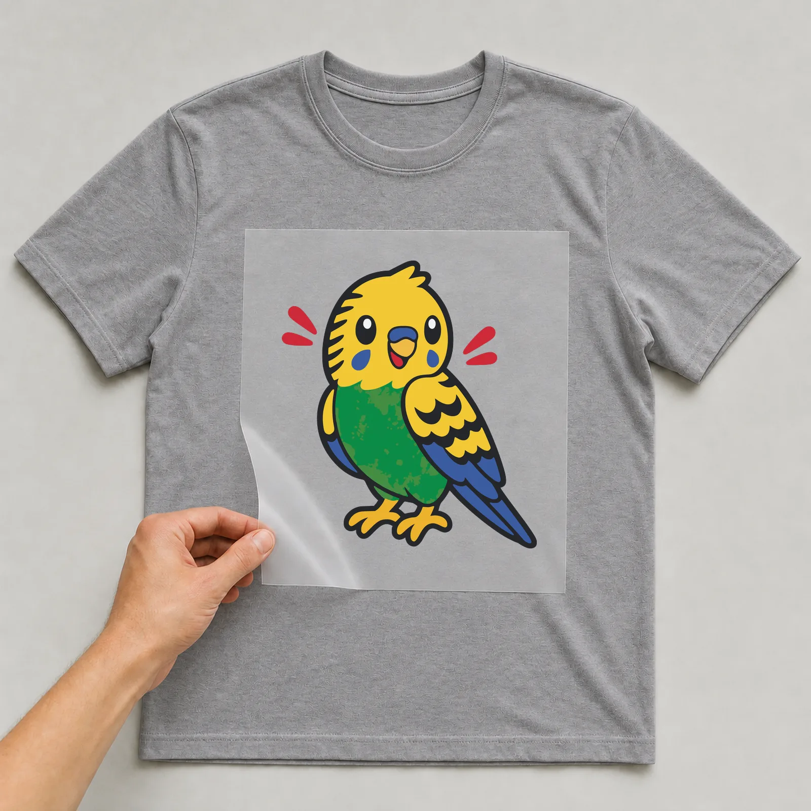 Bügelbild Wellensittich im Comic-Stil auf grauem T-Shirt, Folie wird aufgelegt