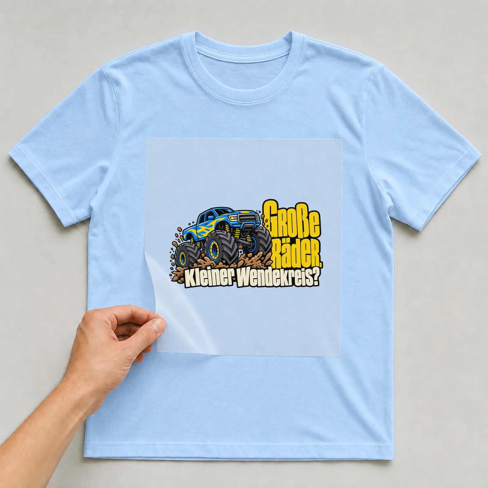 Bügelbild „Große Räder. Kleiner Wendekreis?“ auf hellblauem T-Shirt, Folie wird aufgelegt