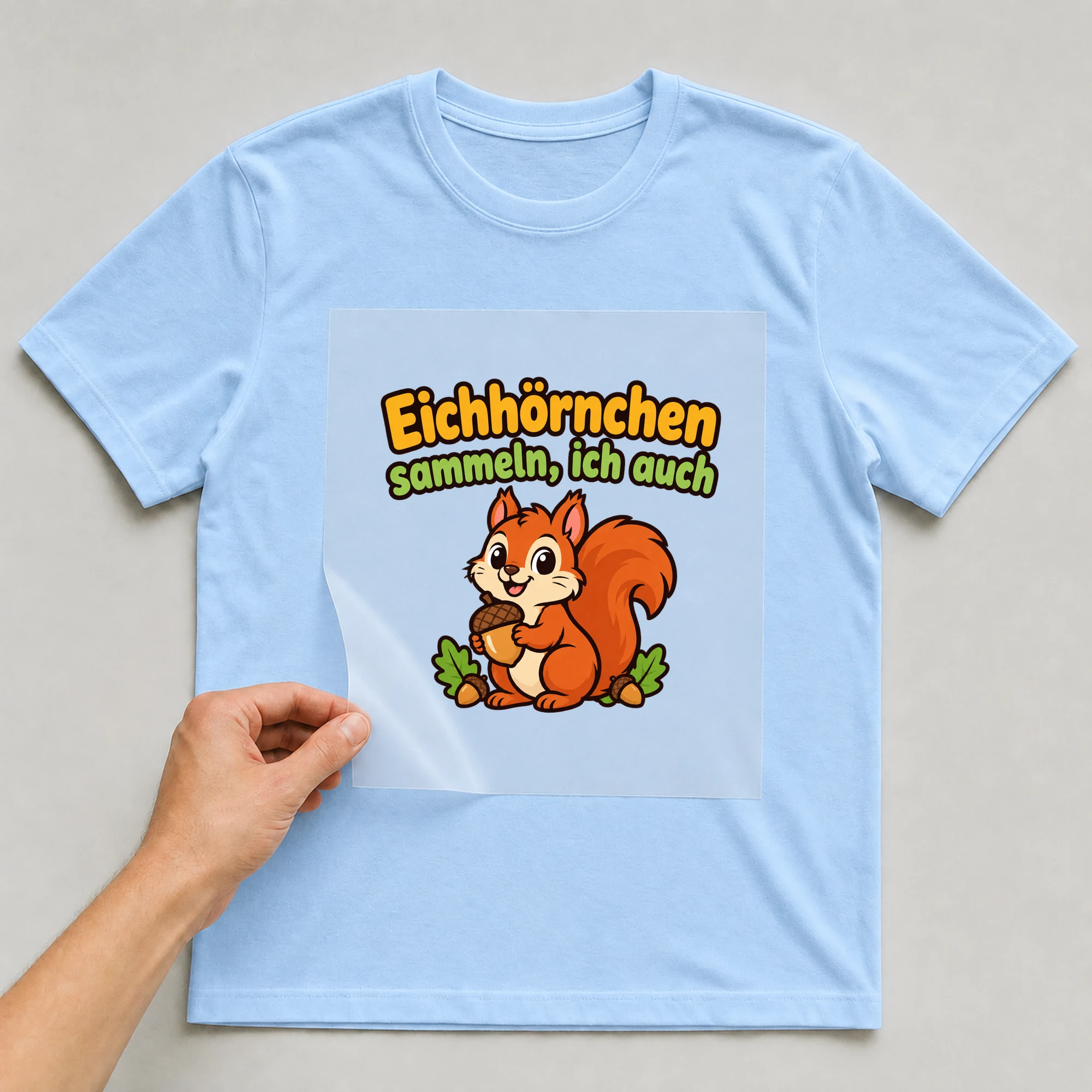 Bügelbild „Eichhörnchen sammeln, ich auch“ auf babyblauem T-Shirt, Folie wird aufgelegt