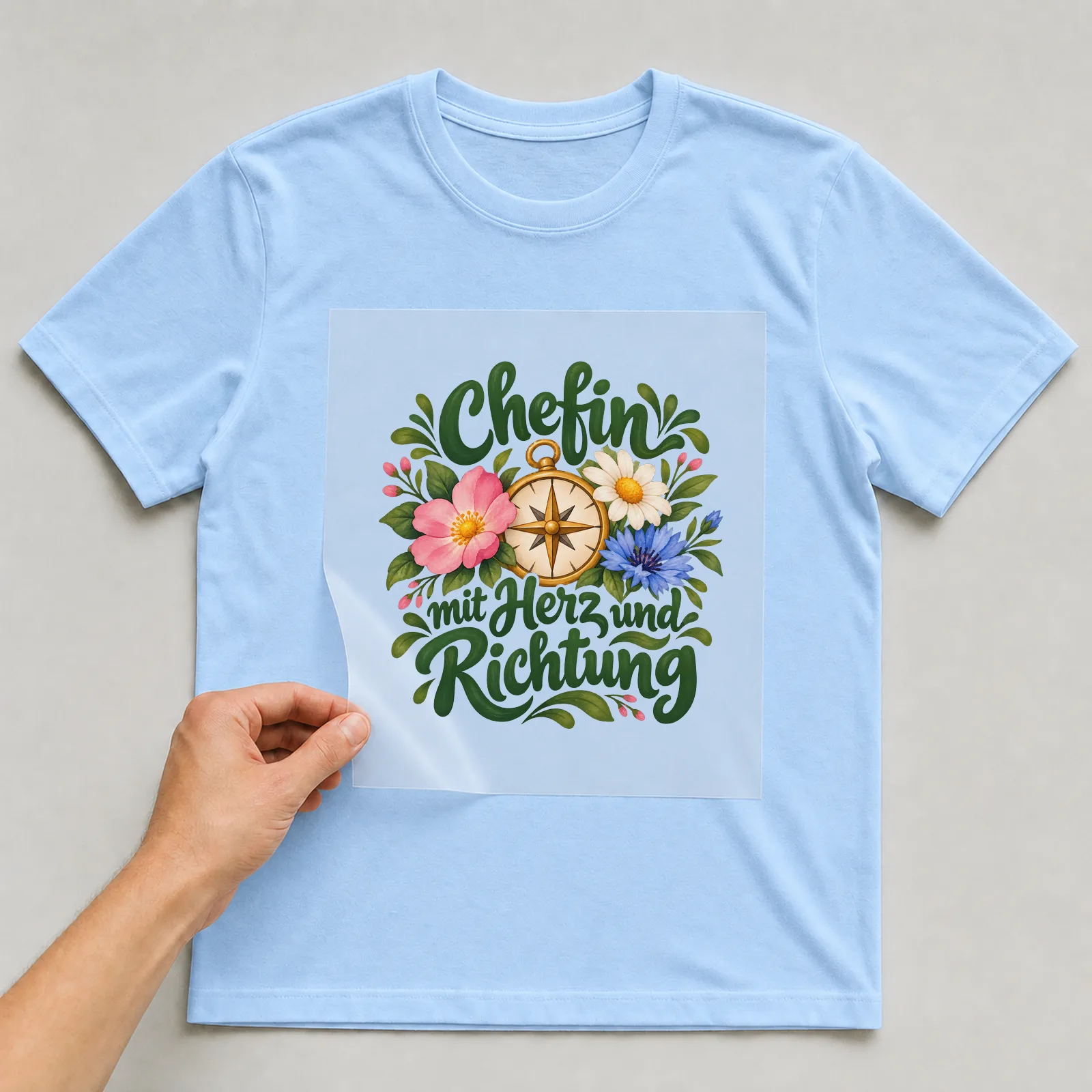 Bügelbild „Chefin mit Herz und Richtung“ auf hellblauem T-Shirt, Folie wird aufgelegt
