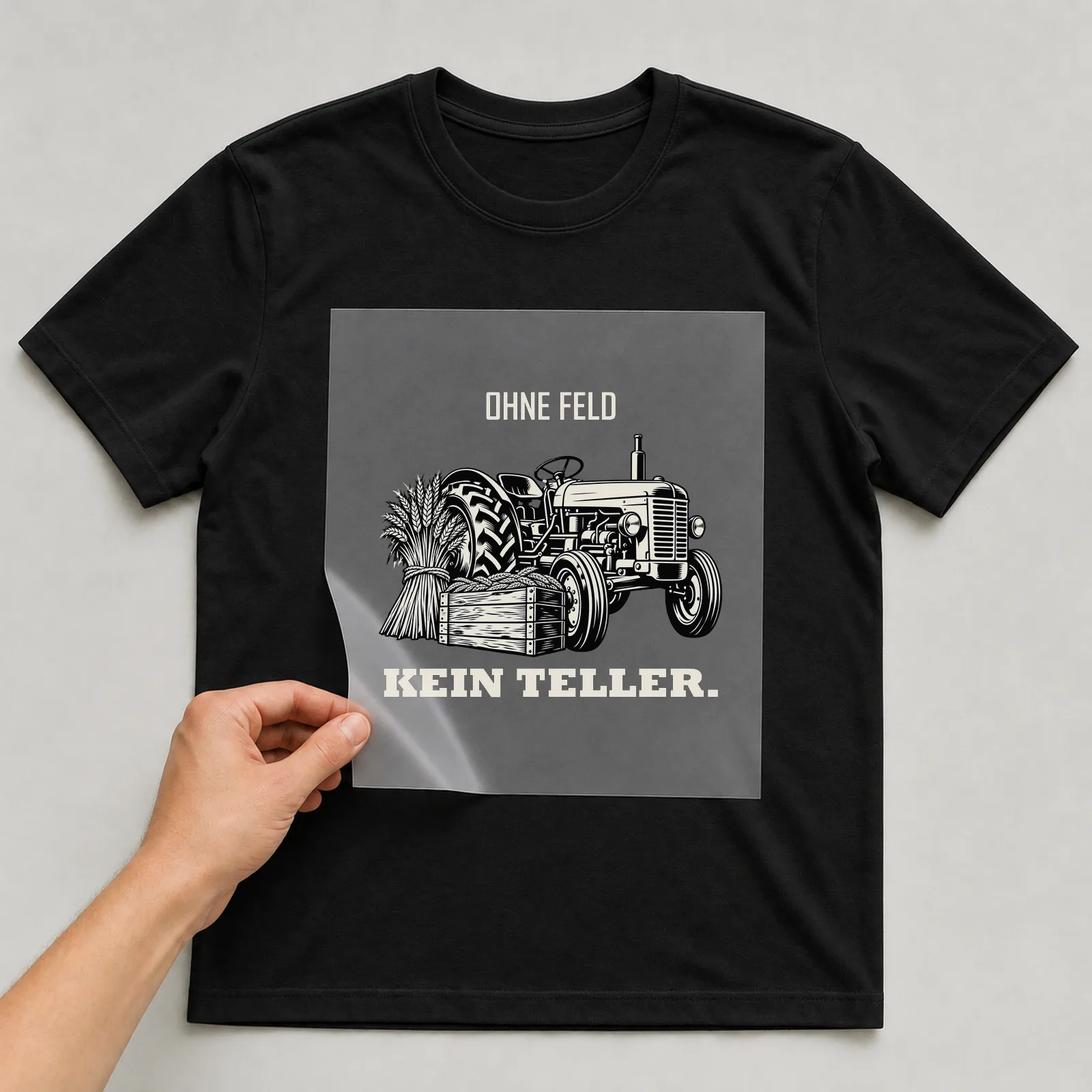 Bügelbild „Ohne Feld kein Teller“ auf schwarzem T-Shirt, Folie wird aufgelegt