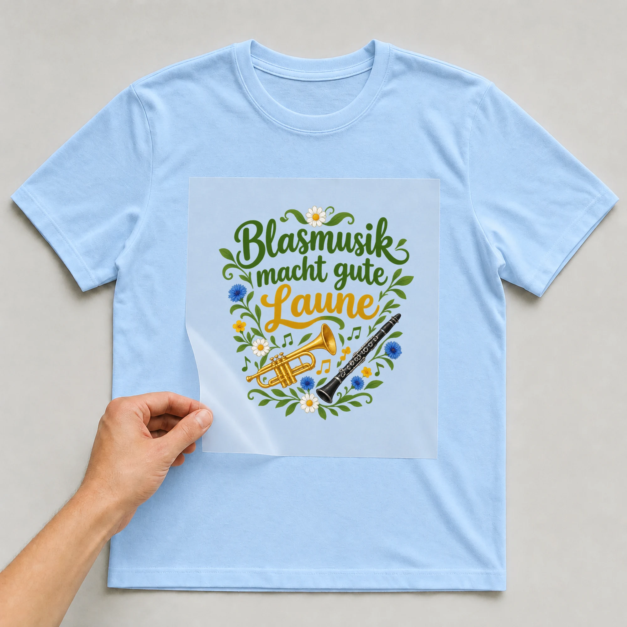 Bügelbild „Blasmusik macht gute Laune“ auf babyblauem T-Shirt, Folie wird aufgelegt