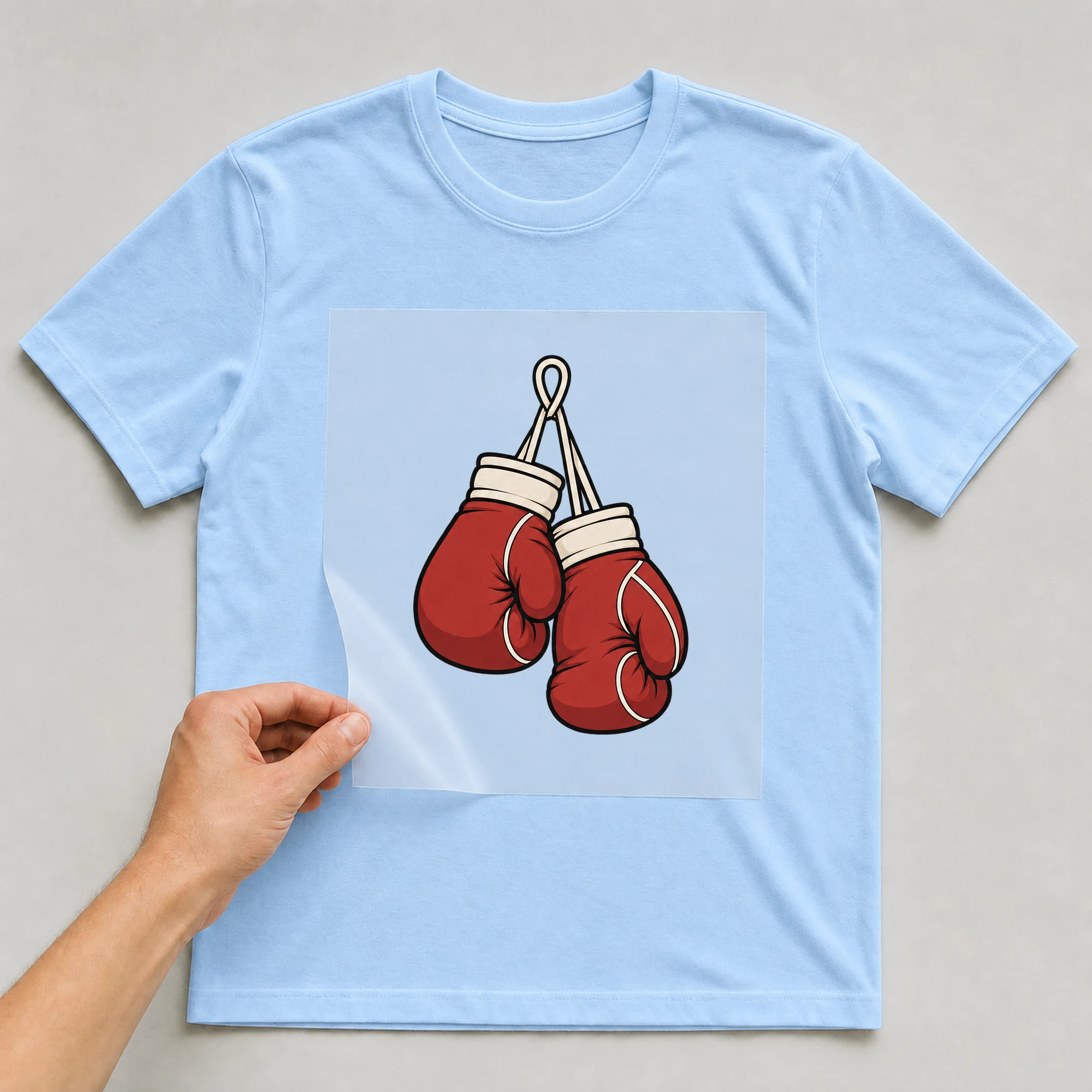 Bügelbild „Boxhandschuhe“ auf babyblauem T-Shirt, Folie wird aufgelegt