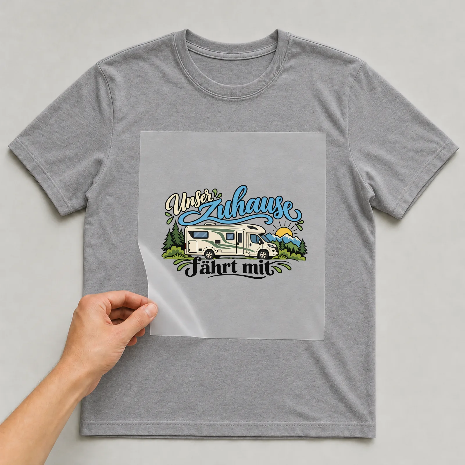 Bügelbild „Unser Zuhause fährt mit“ auf grauem T-Shirt, Folie wird aufgelegt