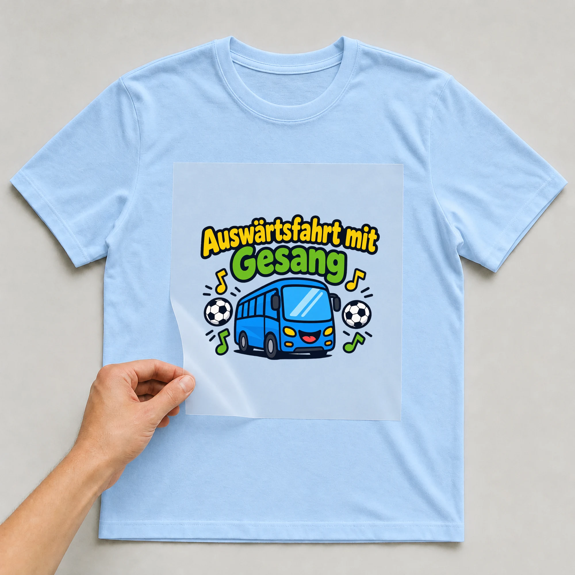 Bügelbild „Auswärtsfahrt mit Gesang“ auf babyblauem T-Shirt, Folie wird aufgelegt