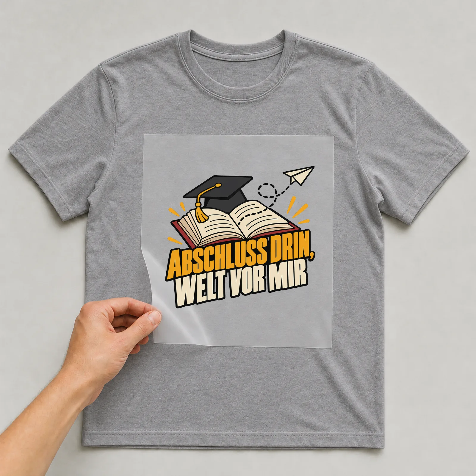 Bügelbild „Abschluss drin, Welt vor mir“ auf grauem T-Shirt, Folie wird aufgelegt