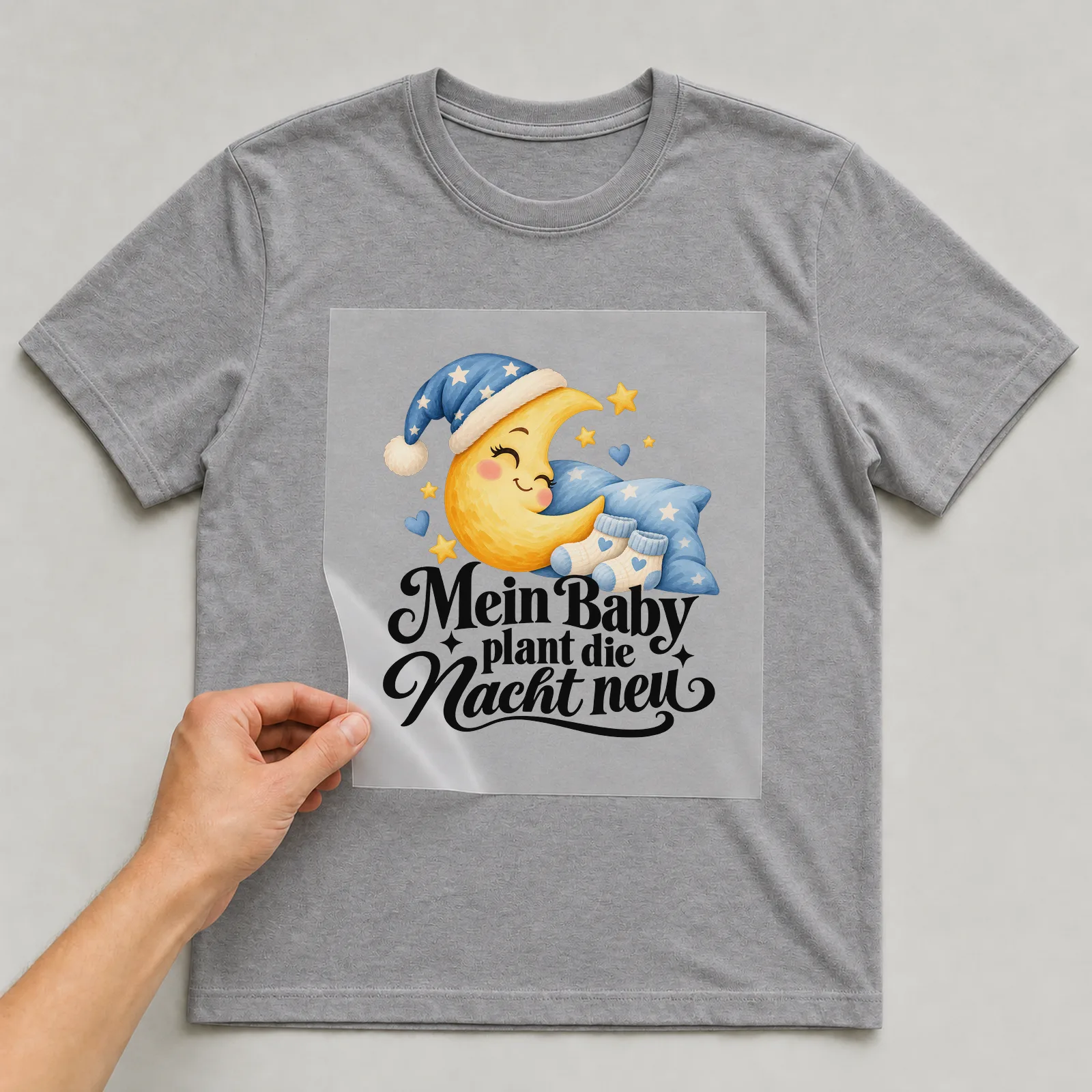 Bügelbild „Mein Baby plant die Nacht neu“ auf grauem T-Shirt, Folie wird aufgelegt