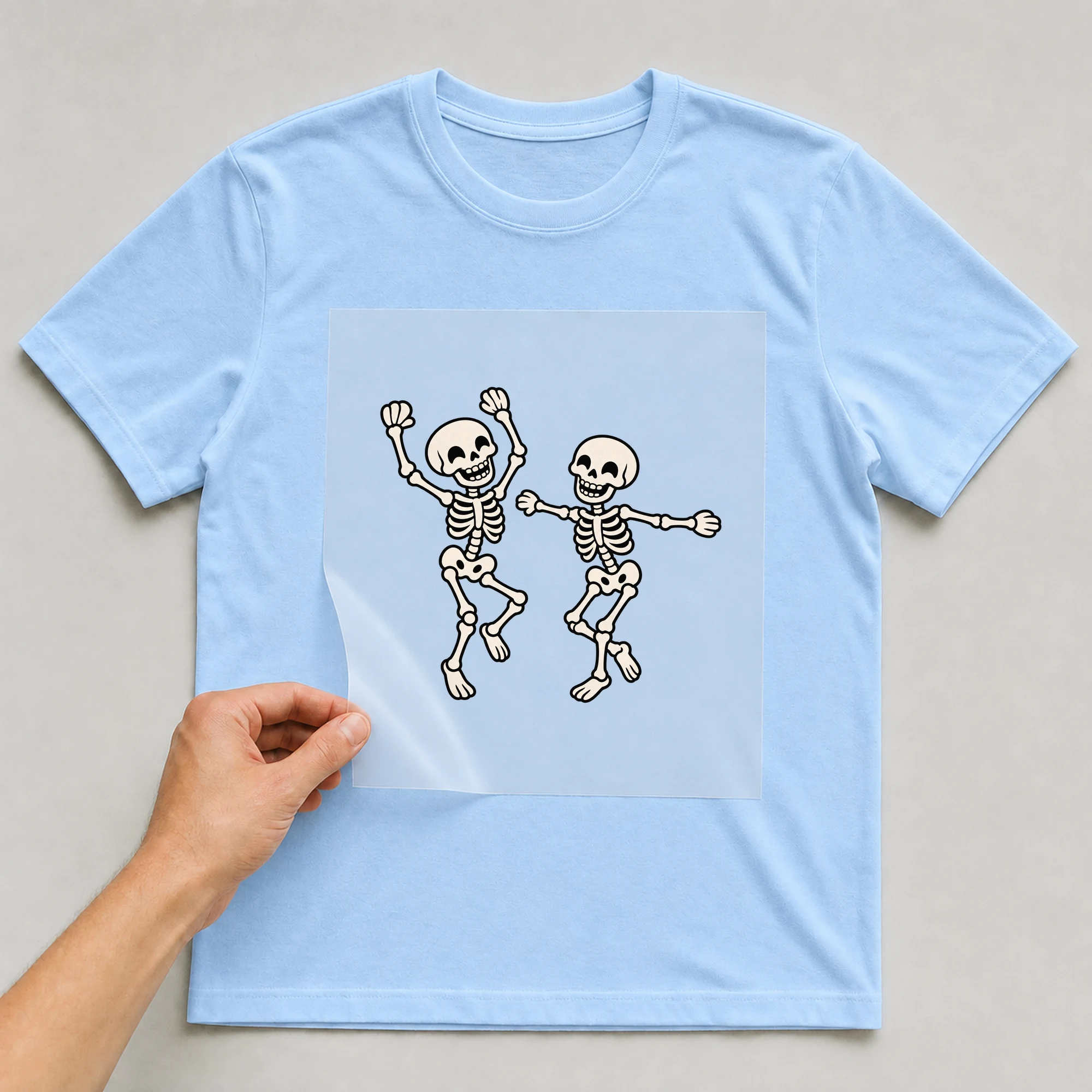 Bügelbild „Tanzende Skelette“ auf babyblauem T-Shirt, Folie wird aufgelegt