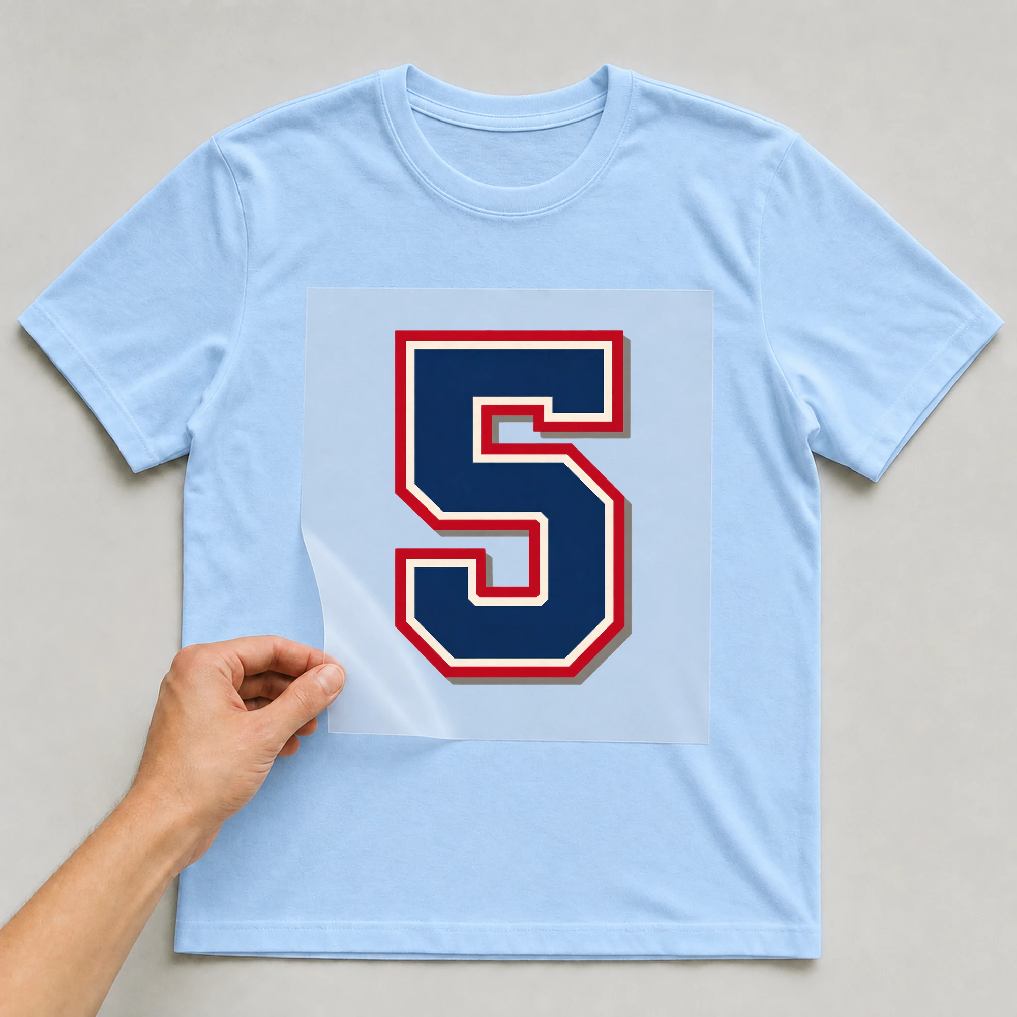 Bügelbild „Zahl 5 im Retro-College-Stil“ auf babyblauem T-Shirt, Folie wird aufgelegt