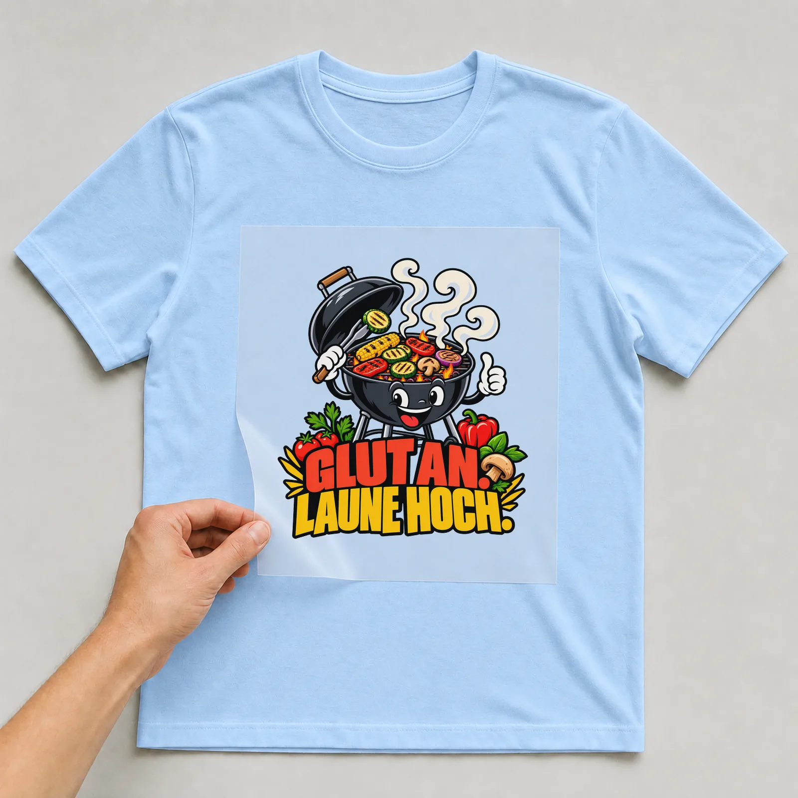Bügelbild „Glut an. Laune hoch.“ auf hellblauem T-Shirt, Folie wird aufgelegt