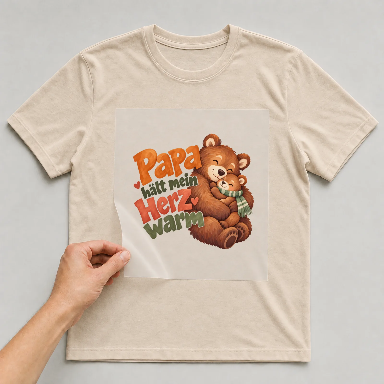 Bügelbild „Papa hält mein Herz warm“ auf beigem T-Shirt, Folie wird aufgelegt