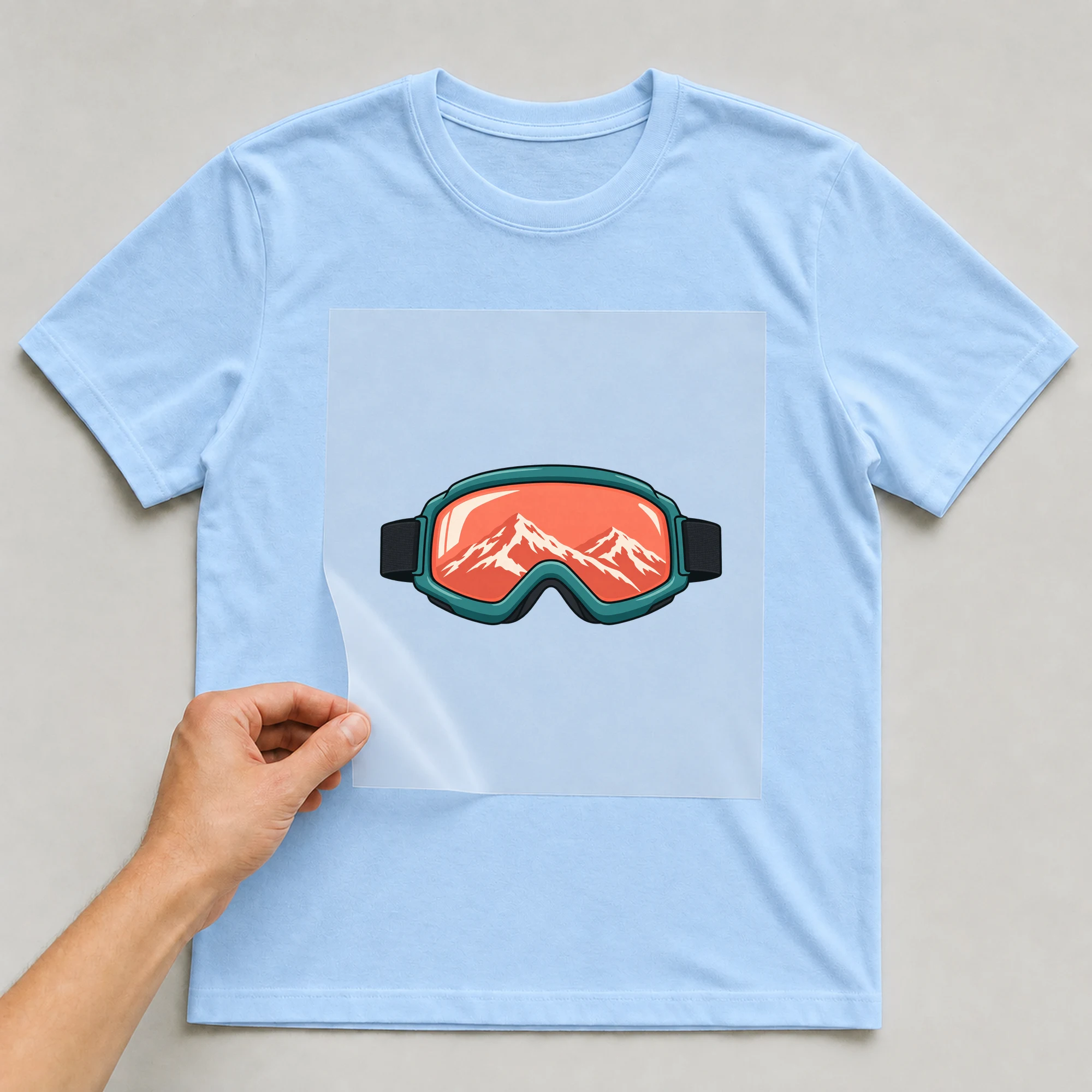 Bügelbild „Snowboarding Logo Brille“ auf babyblauem T-Shirt, Folie wird aufgelegt
