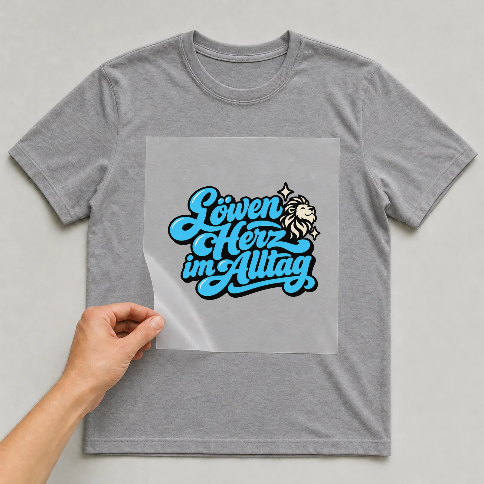 Bügelbild „Löwenherz im Alltag“ auf grauem T-Shirt, Folie wird aufgelegt